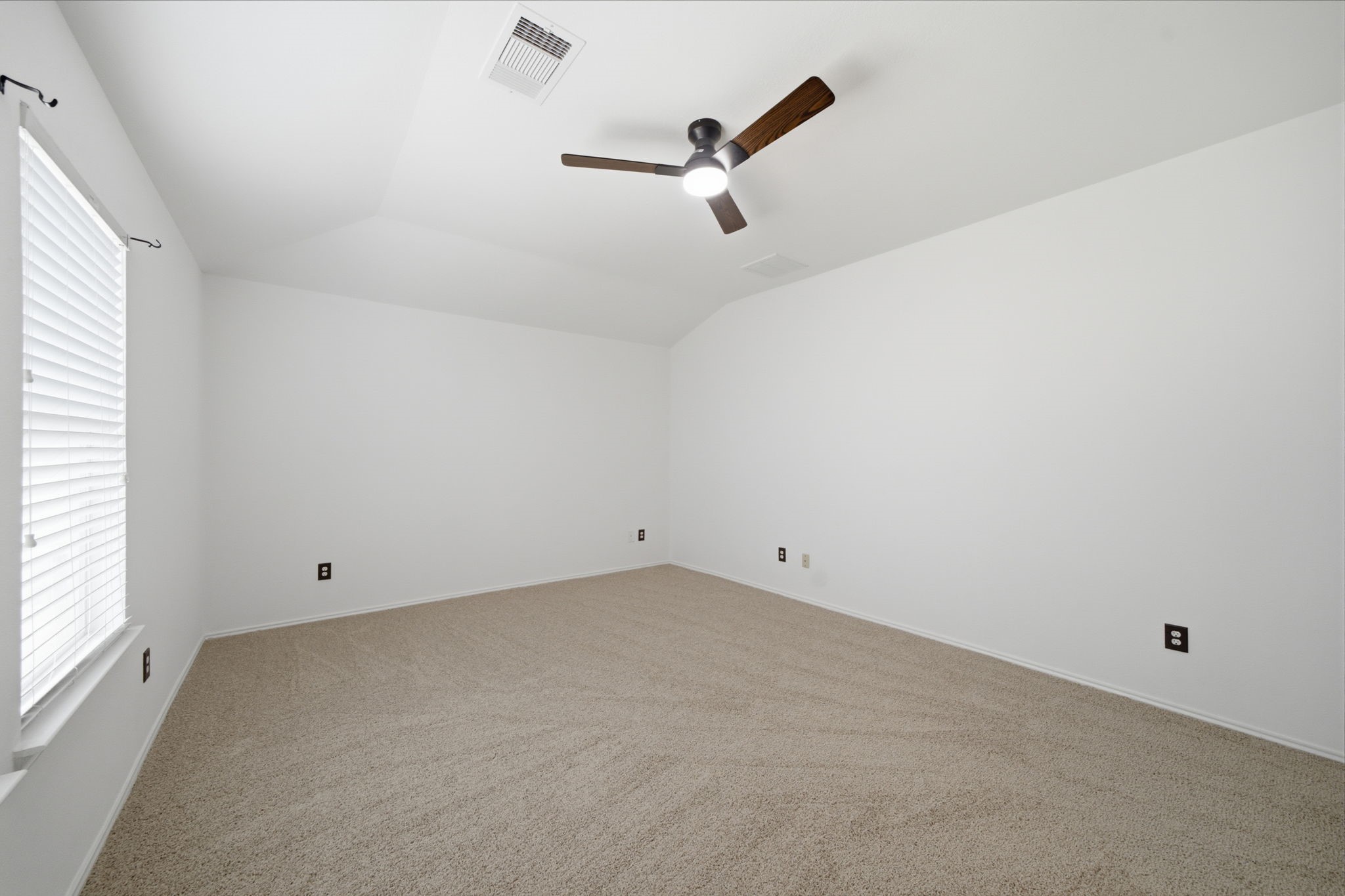 Vaulted ceilings and soft carpet flooring highlight this versatile secondary bedroom. A dark wood-blade ceiling fan and wide window create a comfortable, airy space ready for any bedroom arrangement.