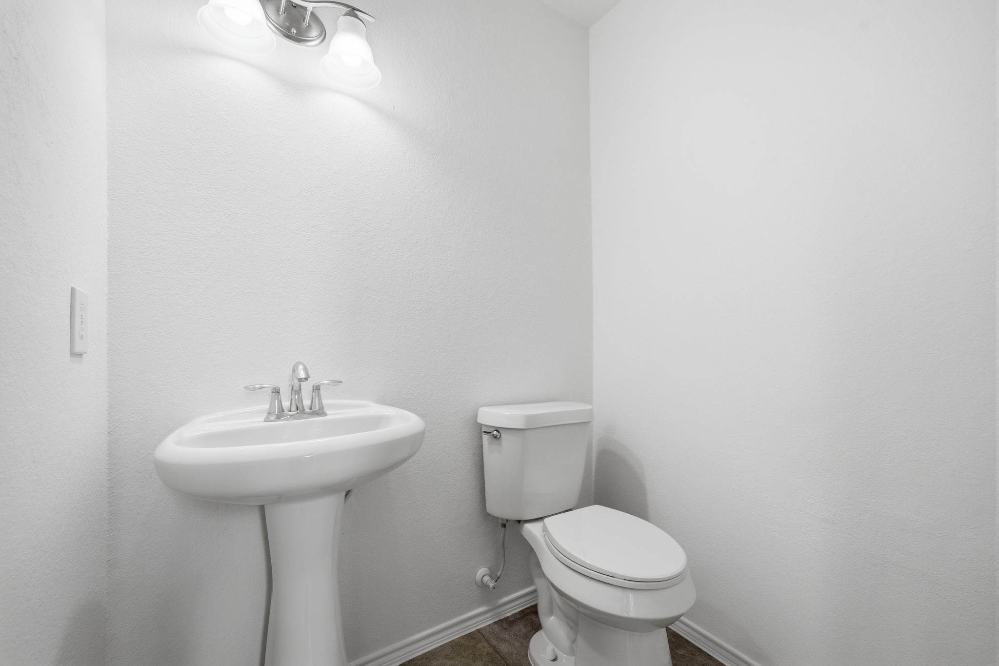 Tucked away for convenience, this half bath features a pedestal sink with sleek chrome fixtures and durable tile flooring.