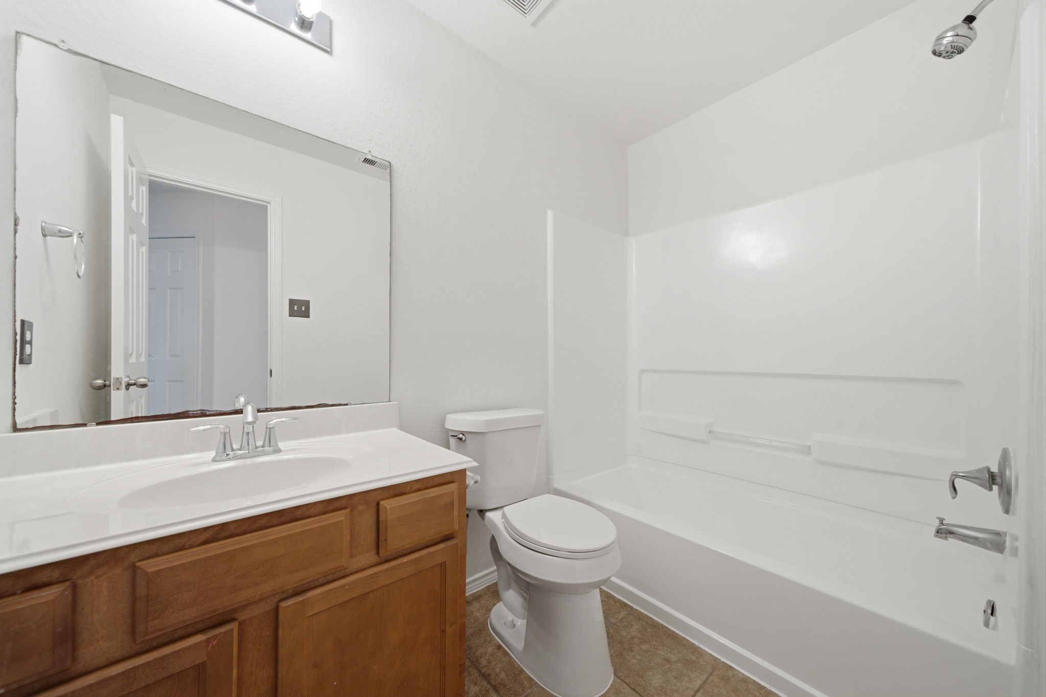 Tiled flooring and a full tub/shower combination with a durable white surround define this functional secondary bathroom. A rich wood vanity provides storage beneath an extended mirror and bright vanity lighting.
