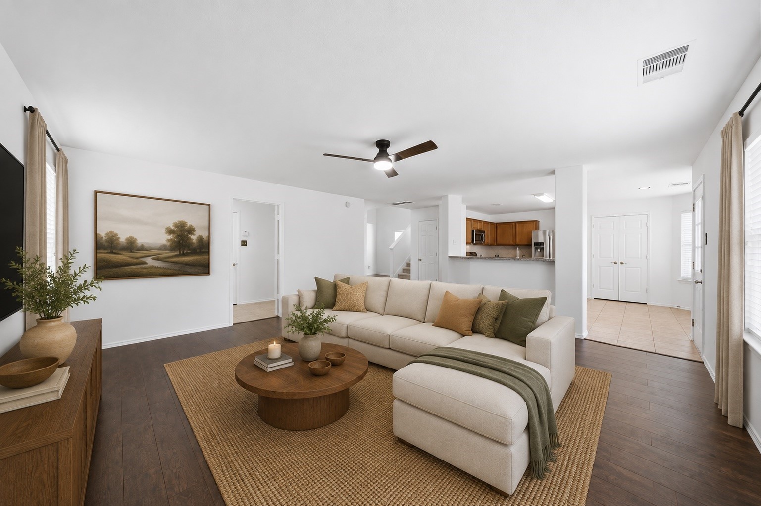 Rich hardwood floors and a modern ceiling fan anchor this spacious first-floor living room with an open layout. Seamless sightlines lead straight past the raised breakfast bar into the adjacent kitchen, creating an effortless flow.