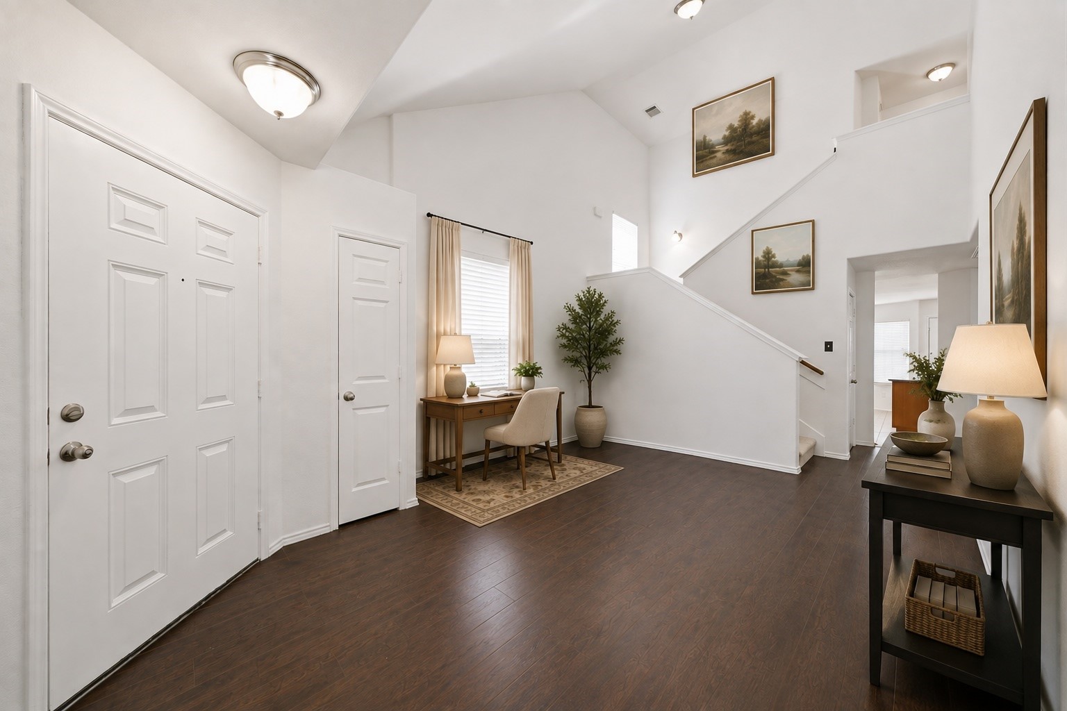 Vaulted ceilings and rich wood-look flooring create an airy welcome in this light-filled foyer. An alcove accommodates a compact desk, while the main staircase leads to the second-floor living spaces. This photo has been virtually staged.