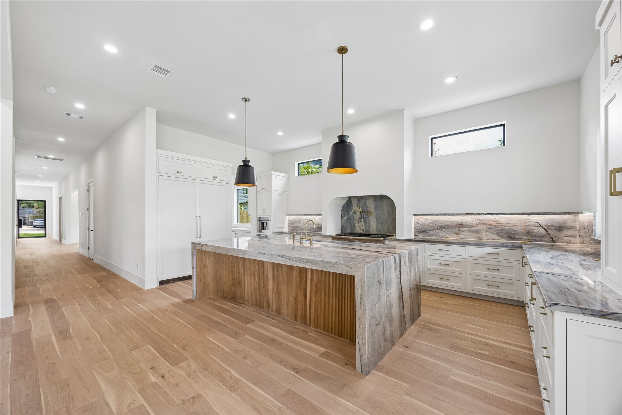 Anchored by a dramatic waterfall island with warm wood detailing, this chefs kitchen blends timeless design with exceptional craftsmanship. Natural stone surfaces, fully inset custom cabinetry, statement lighting, and a panel ready Thermador fridge/freezer combo create a space thats as beautiful as it is thoughtfully designed.