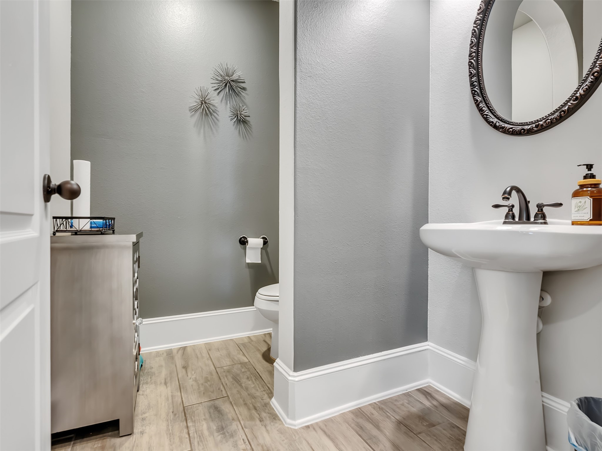 Powder room with pedestal sink and neutral color tones with tile flooring.