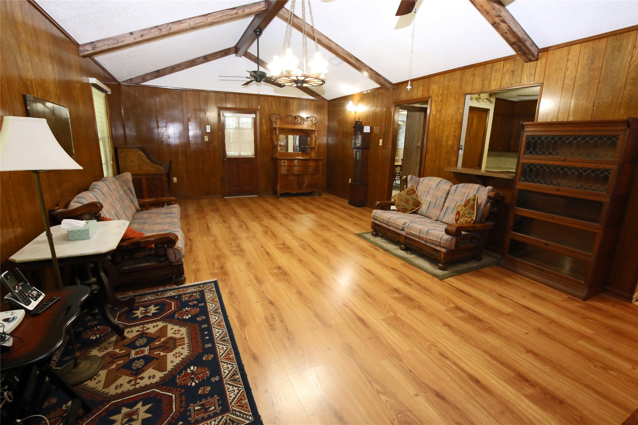 Spacious living room featuring warm wood paneling, vaulted ceilings with exposed beams, and elegant hardwood floors. Perfect for cozy gatherings and relaxation.