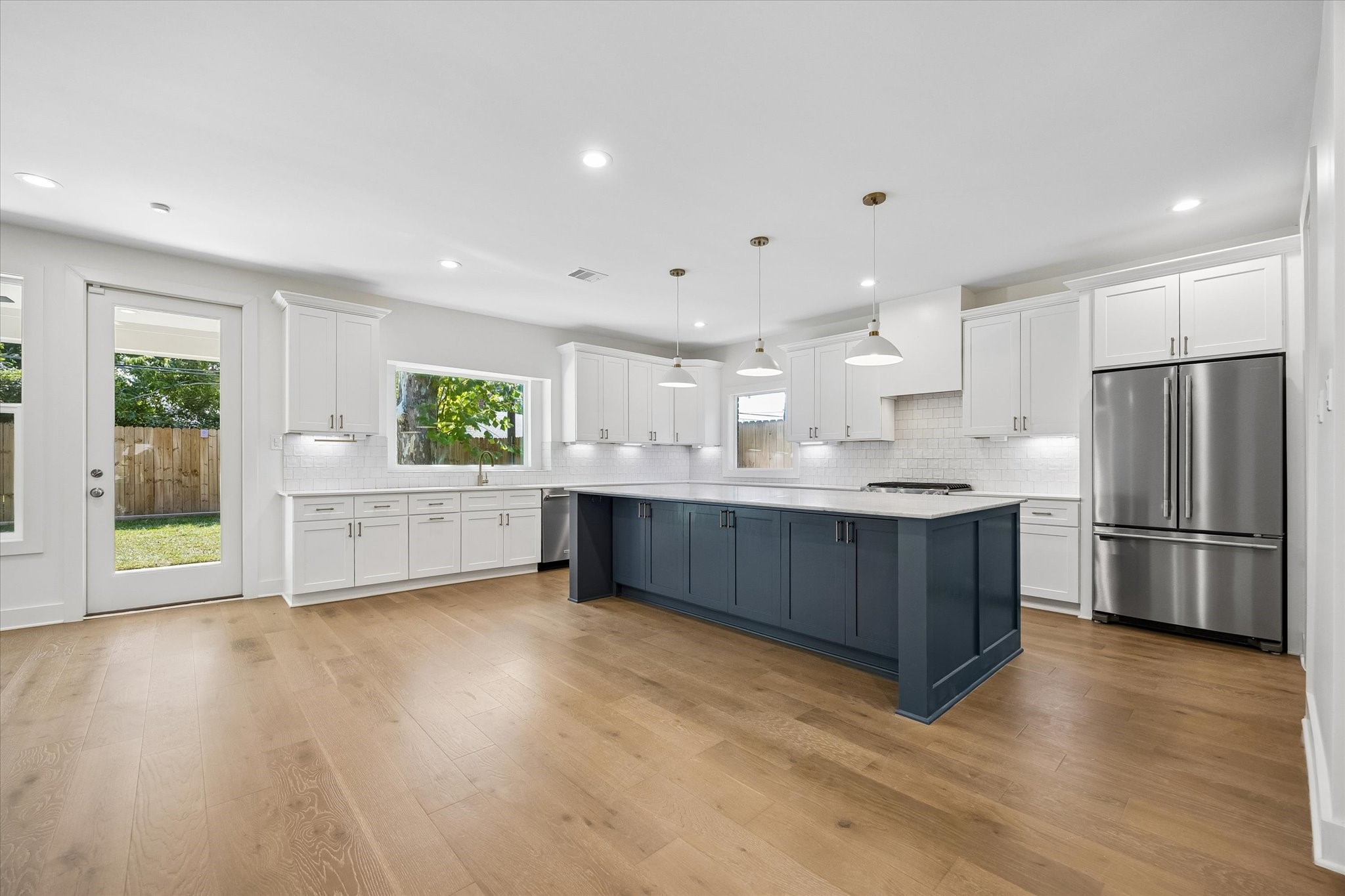 The kitchen features a contemporary design with ample cabinetry and a generous island, providing both functionality and style. Large windows ensure the space is bathed in natural light, while pendant lights above the island add a modern touch. This kitchen is perfect for both cooking and casual dining.