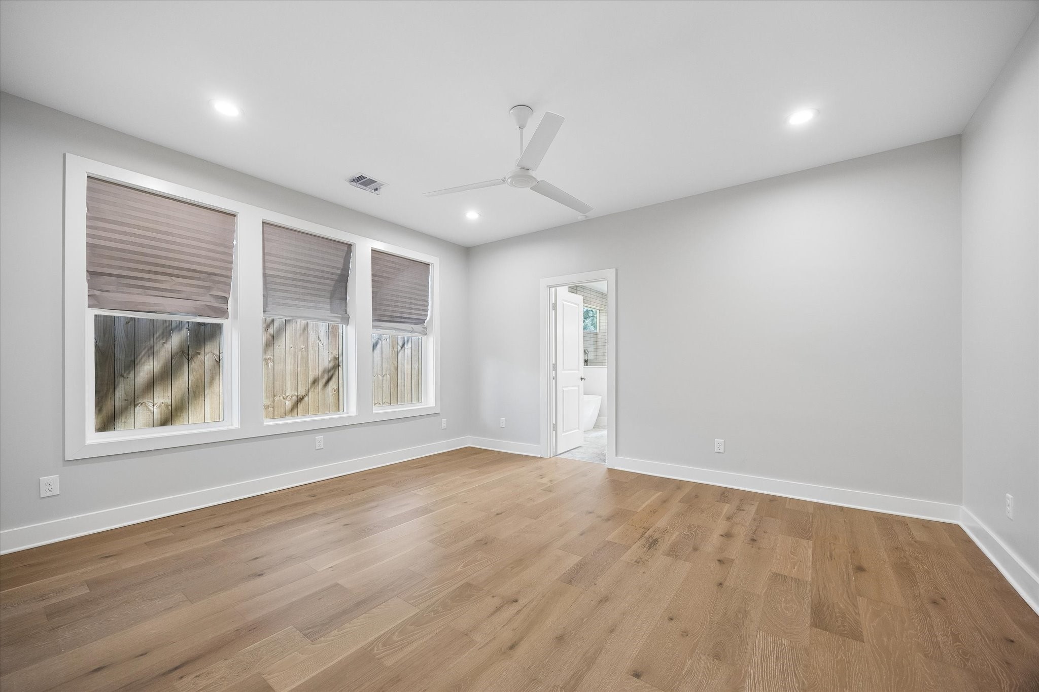 This spacious primary bedroom features large windows, creating a bright and welcoming space. The hardwood floors add a touch of elegance, while the ceiling fan ensures comfort. The room also includes direct access to a luxurious en-suite bathroom.