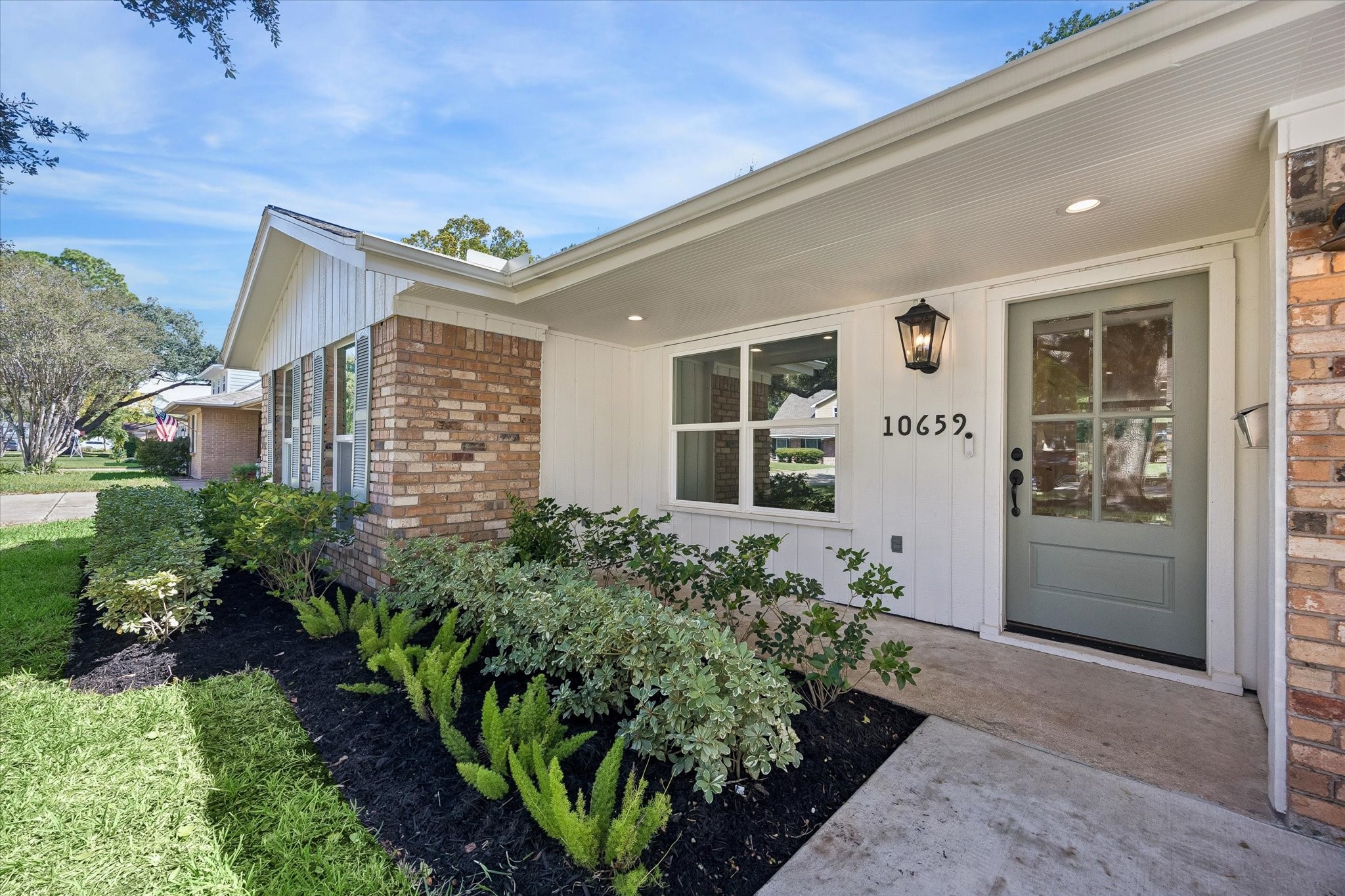 A closer look at the covered front entry highlights the homes thoughtful exterior updates, including fresh landscaping, classic brick detailing and a soft sage front door. Deep overhangs provide a sheltered approach while preserving the homes inviting ranch style character.