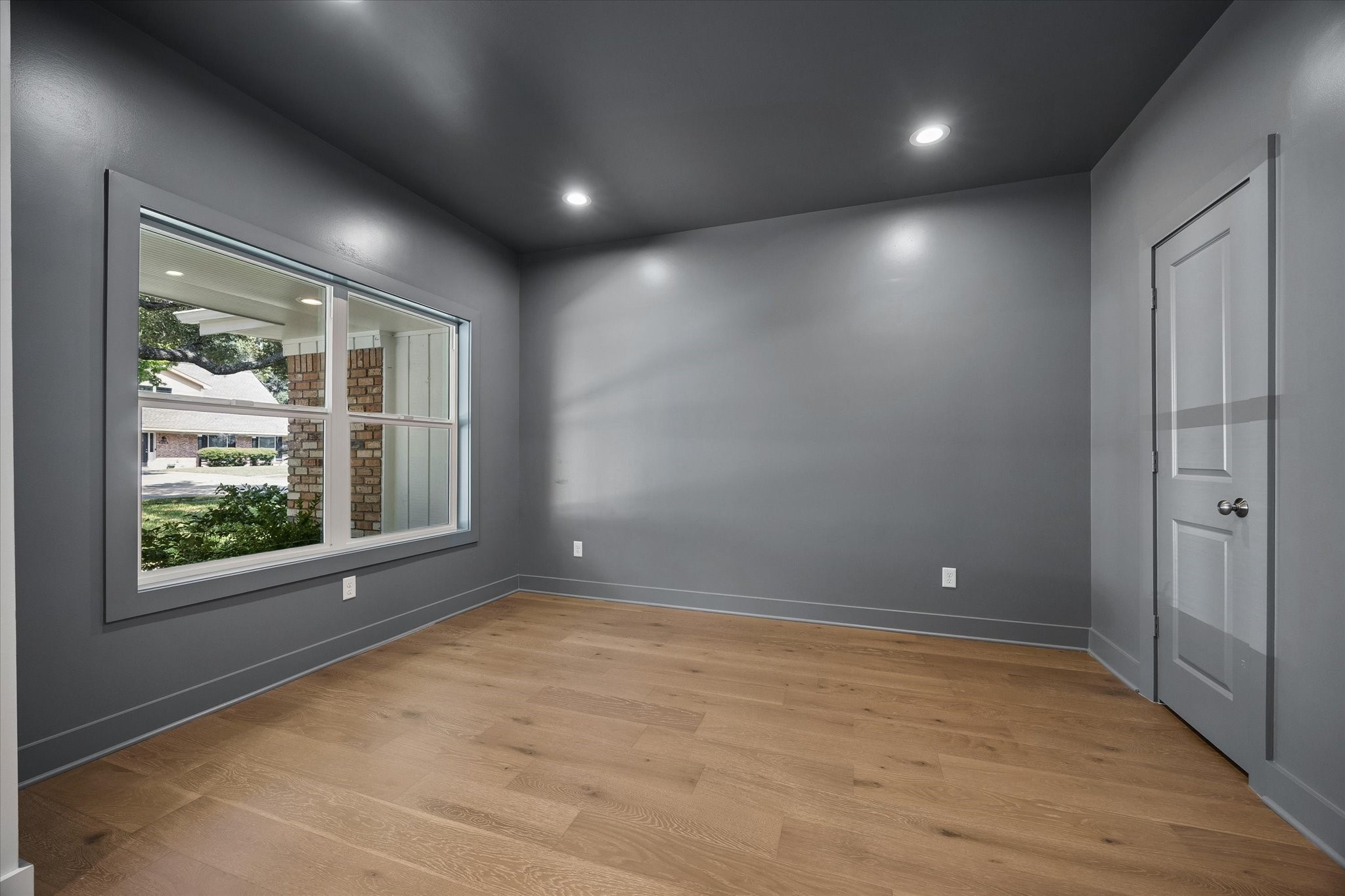 Moody charcoal walls and ceiling give this front room a distinctive, elevated feel, while the oversized window brings in natural light. Well suited for a private home office, study, library or intimate sitting room.