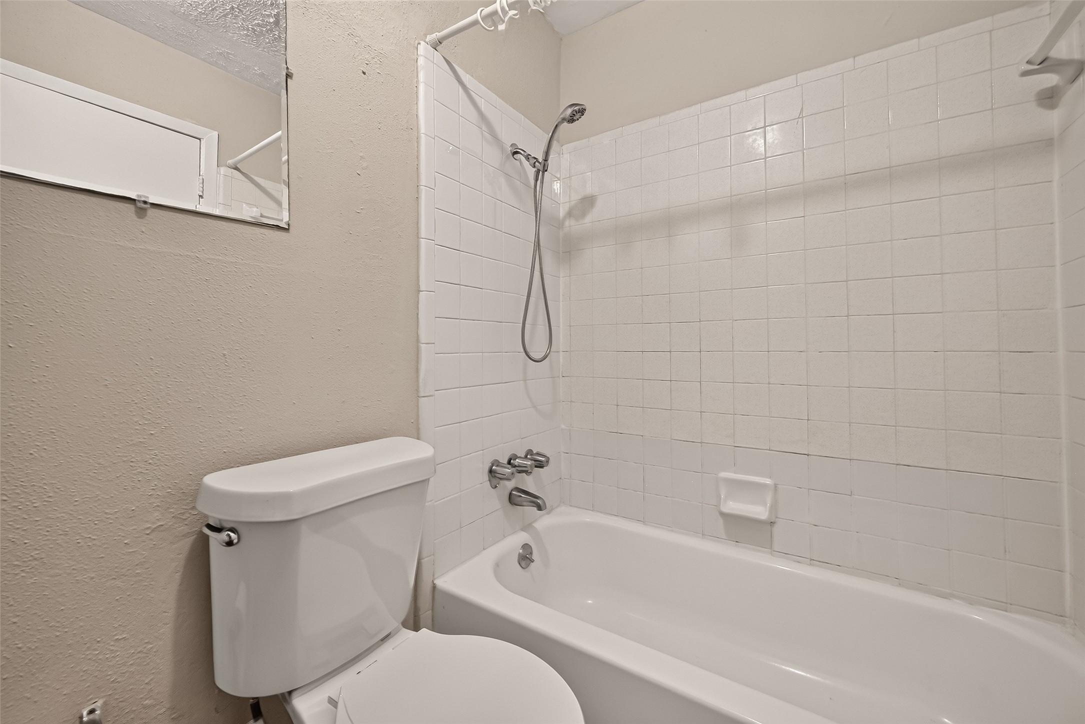 Cozy bathroom with a classic white tiled bathtub and shower combination, complemented by neutral walls for a clean and inviting feel.