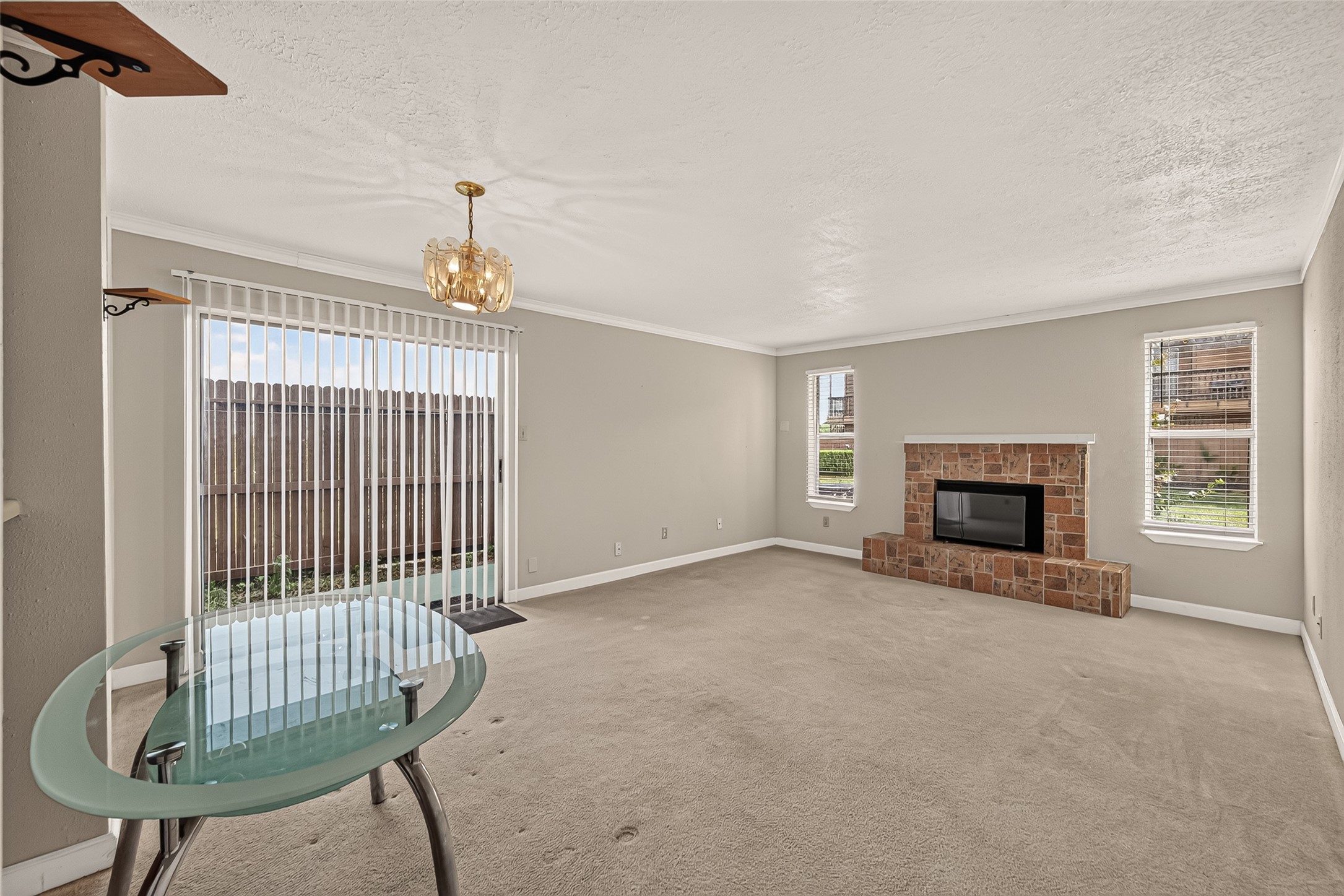 Spacious living area with a cozy brick fireplace and ample natural light from large windows and sliding glass doors, providing easy access to the patio.