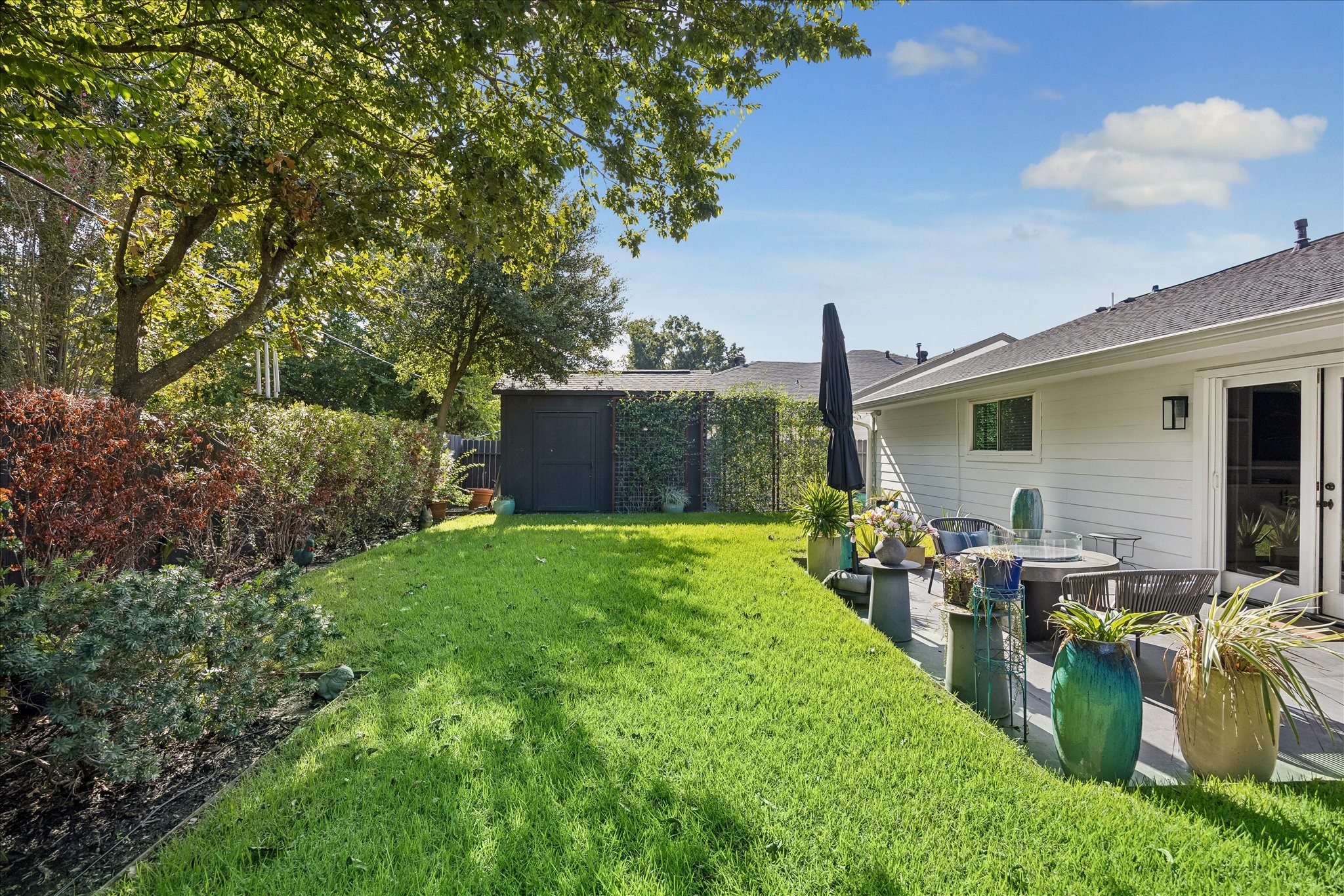 Mature trees frame the expansive lawn, with a welcoming patio and garden shed completing this peaceful outdoor retreat.