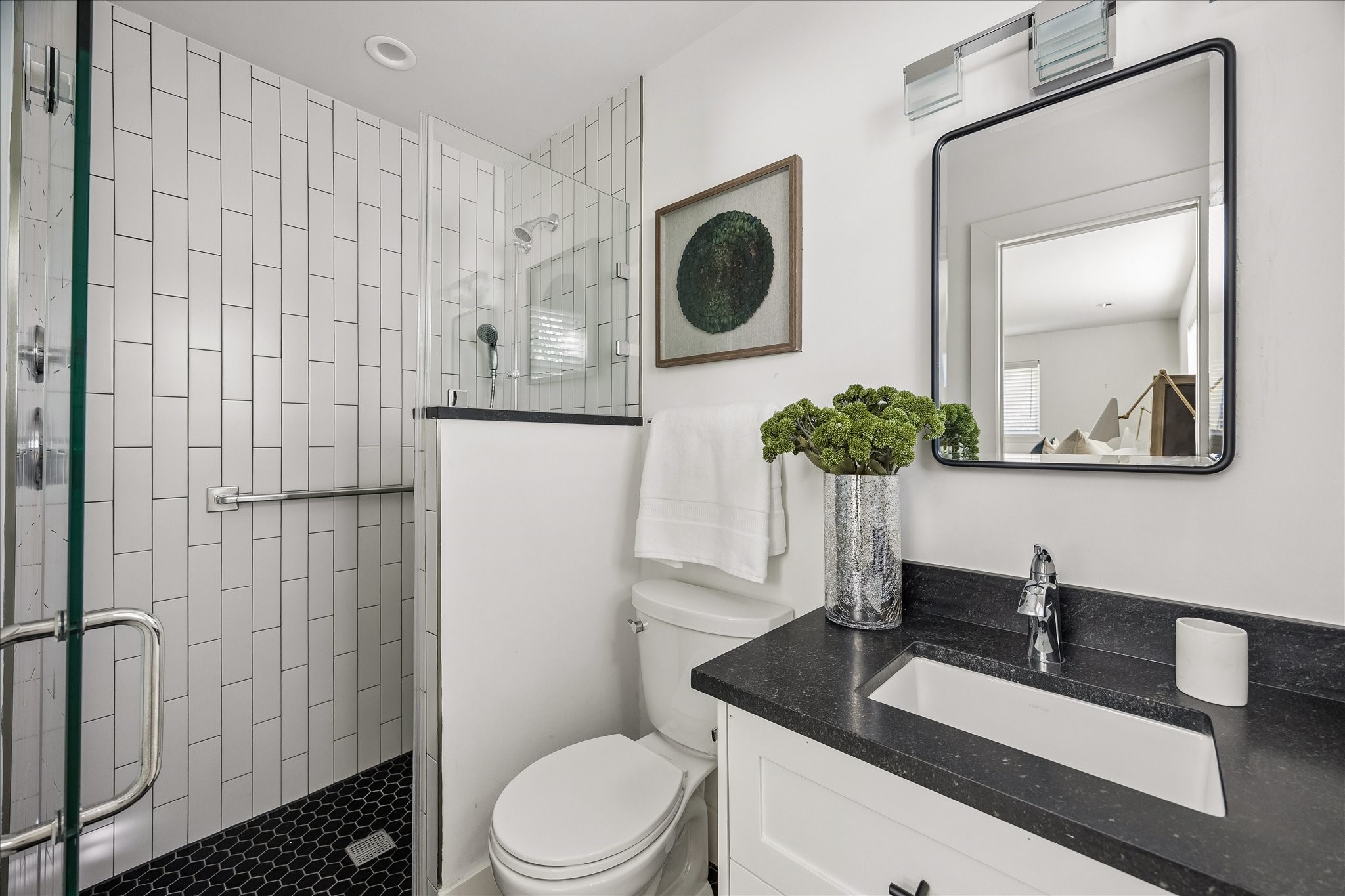 Beautifully updated primary bath featuring crisp white tile, a glass-enclosed shower, and contrasting dark countertops.