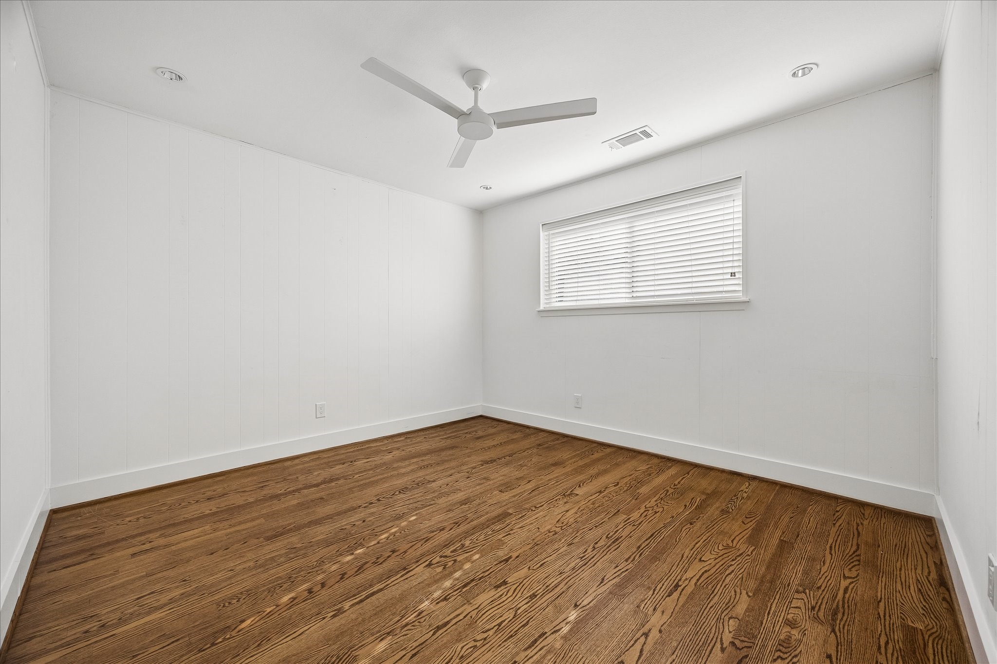 Fresh white painted walls, hardwood flooring, and a ceiling fan lend understated charm to this secondary bedroom.