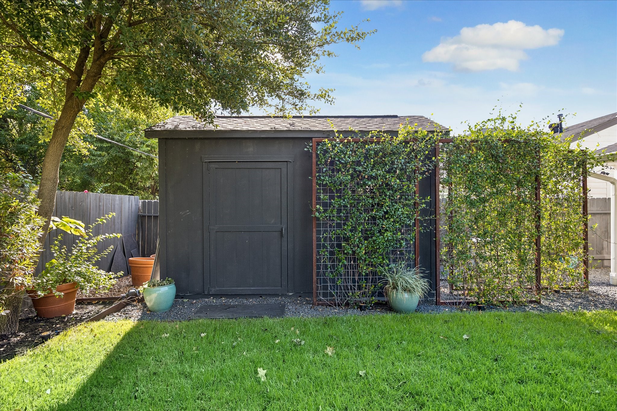 Tucked beneath mature trees, a charming garden shed with vine-covered trellis provides additional storage and character.