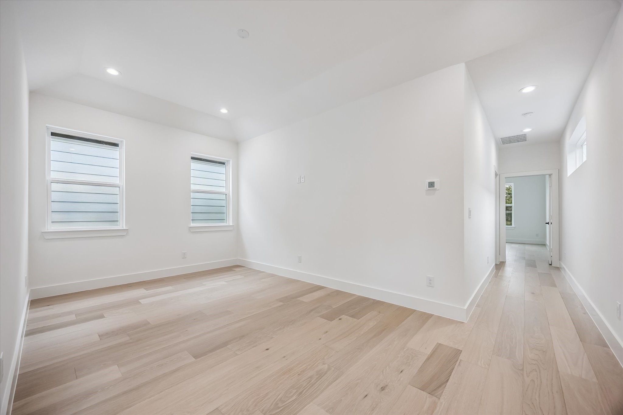 Bright and spacious room with light wood flooring, recessed lighting, and large windows offering plenty of natural light.