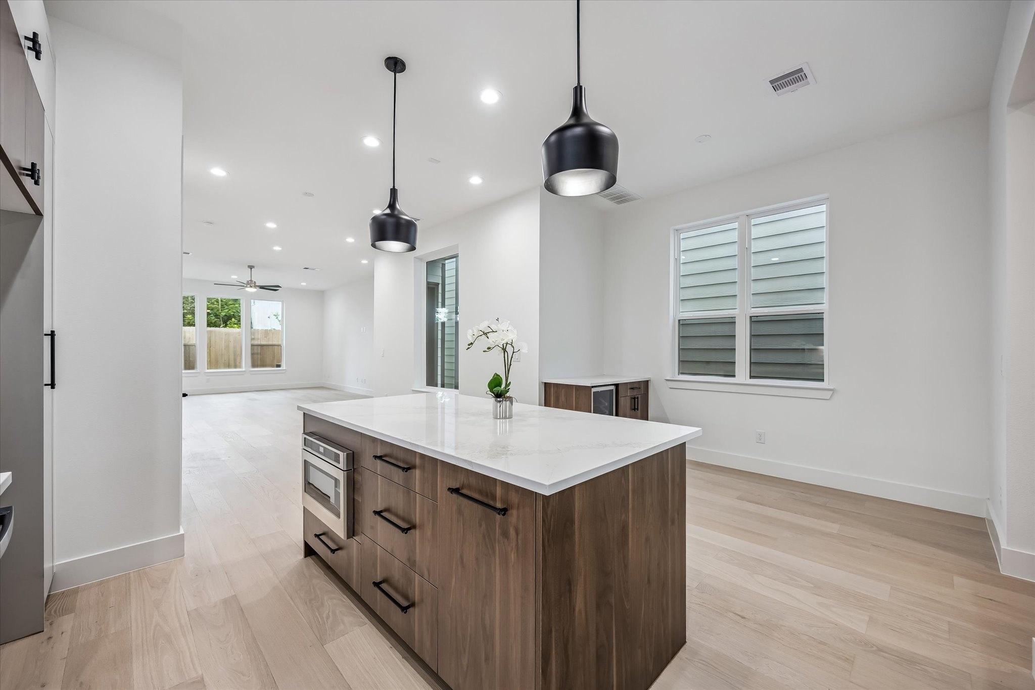Sleek modern kitchen featuring a spacious island with elegant pendant lighting, opening to a bright, airy living area with large windows.