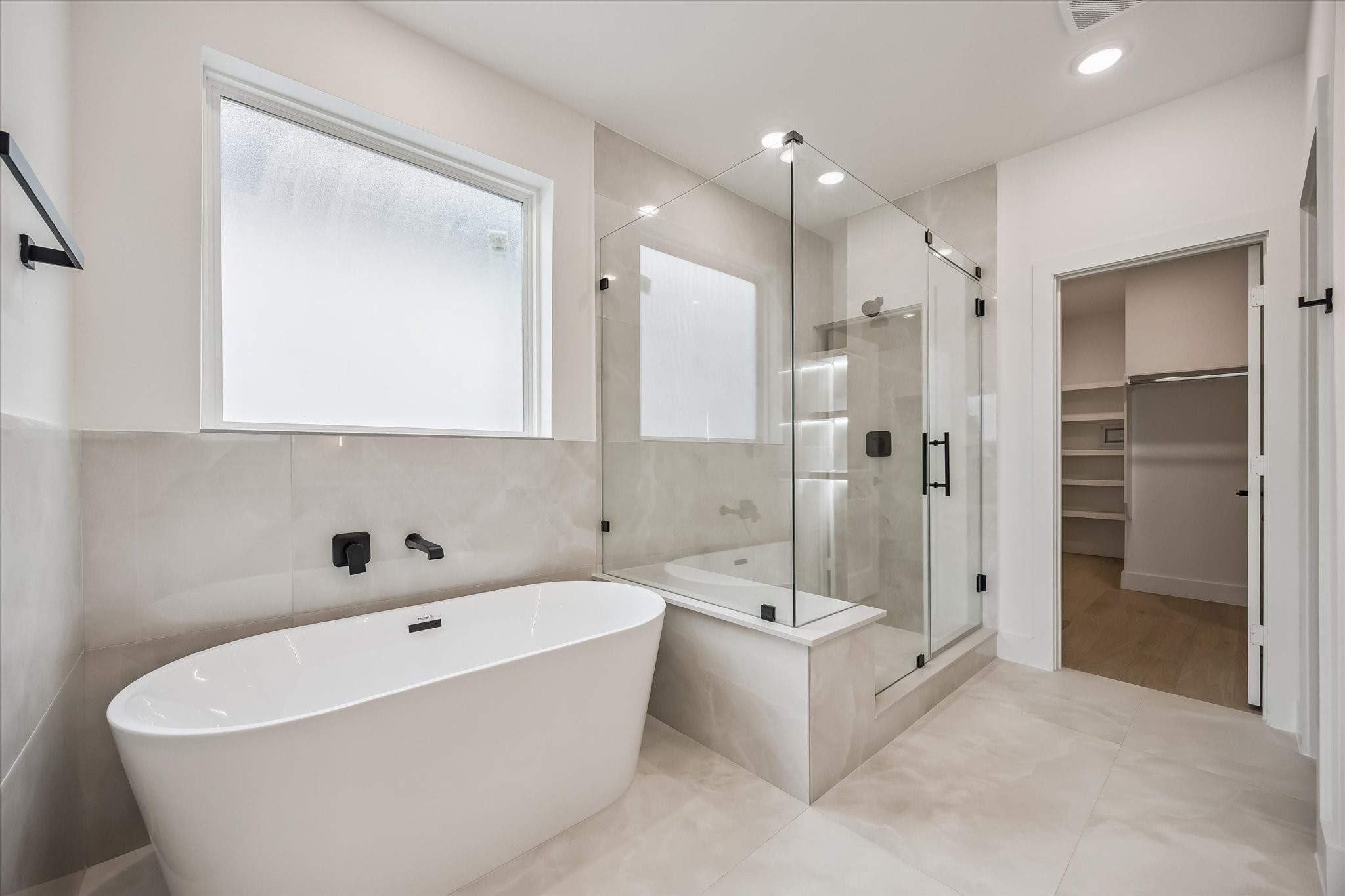 Luxurious bathroom featuring a freestanding tub, glass-enclosed shower, and sleek modern fixtures, seamlessly connected to a spacious walk-in closet.