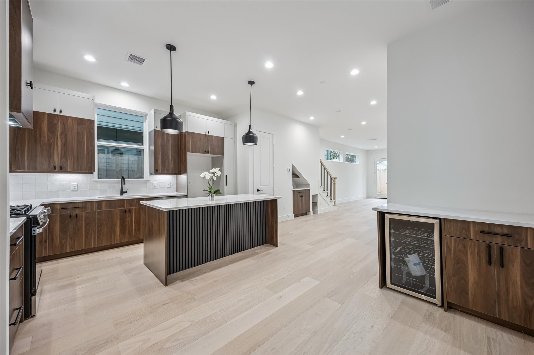 Sleek and modern kitchen featuring an island with pendant lighting, elegant wood cabinetry, and a built-in wine cooler.
