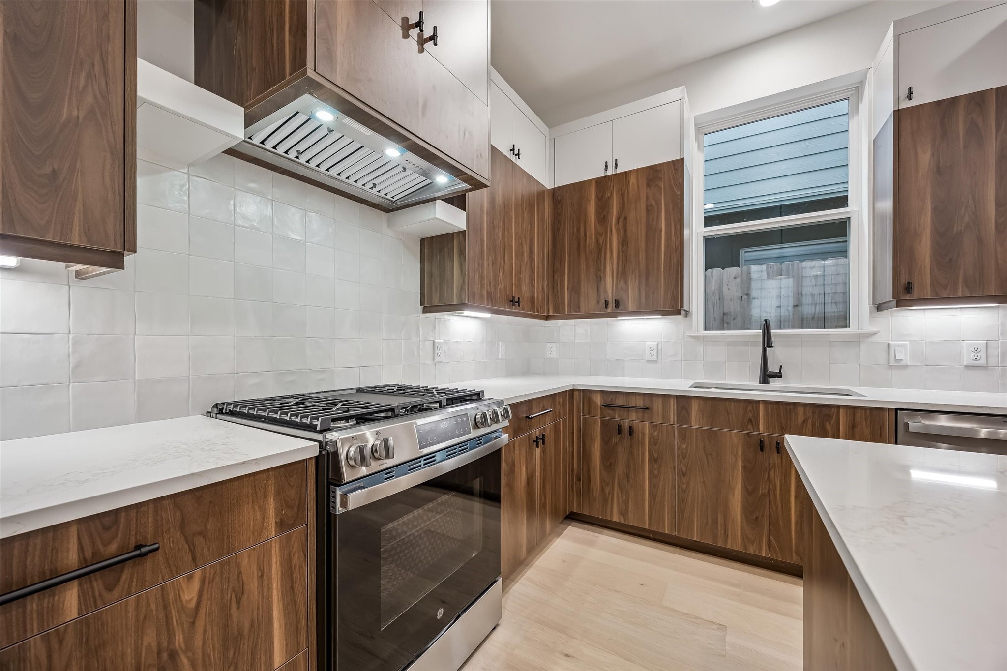 Modern kitchen with sleek wood cabinetry, stainless steel appliances, and elegant white countertops, creating a stylish and functional space.