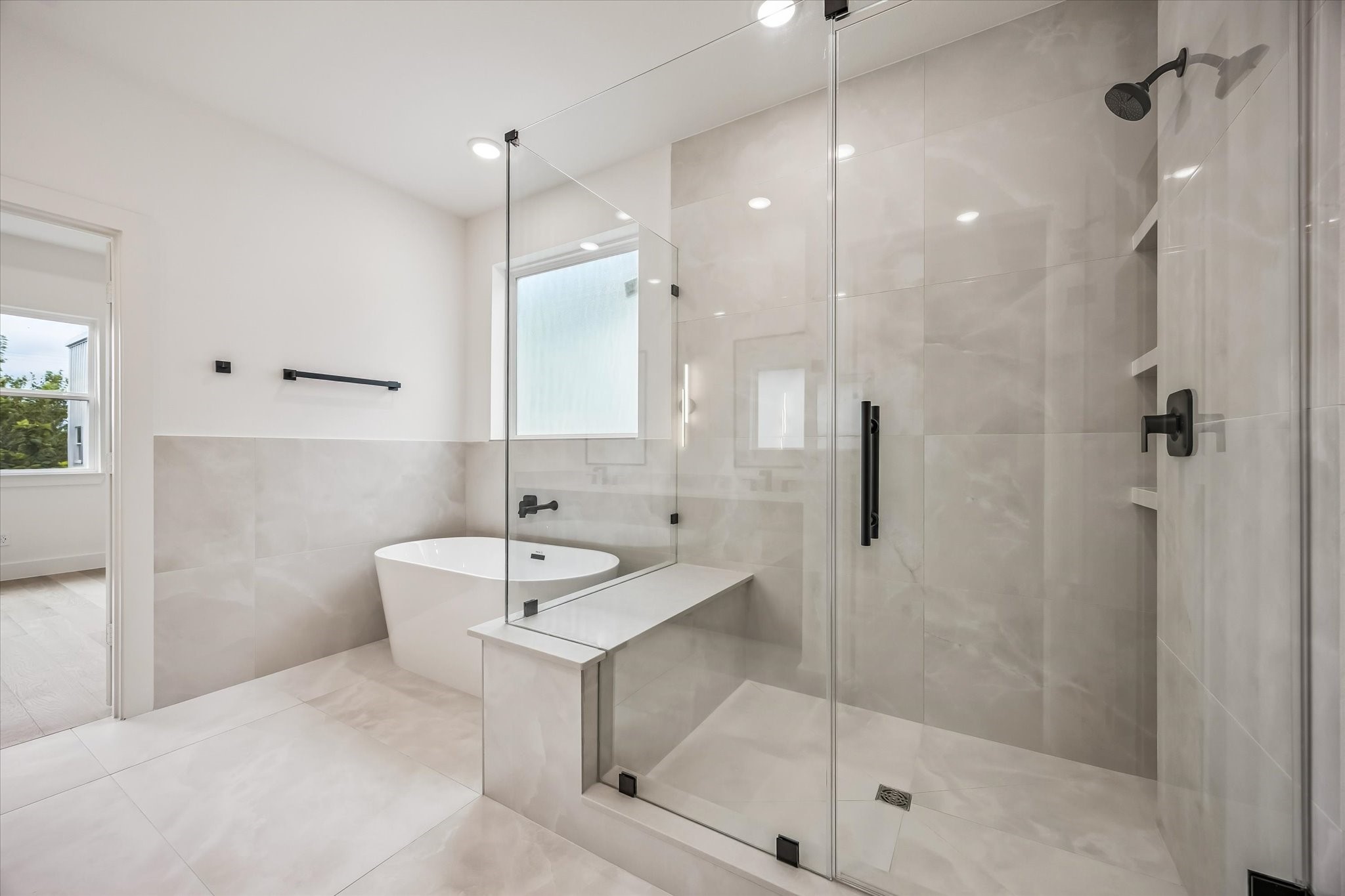 Luxurious bathroom featuring a spacious glass-enclosed shower, elegant soaking tub, and modern fixtures, all accented by sleek tile work and abundant natural light.