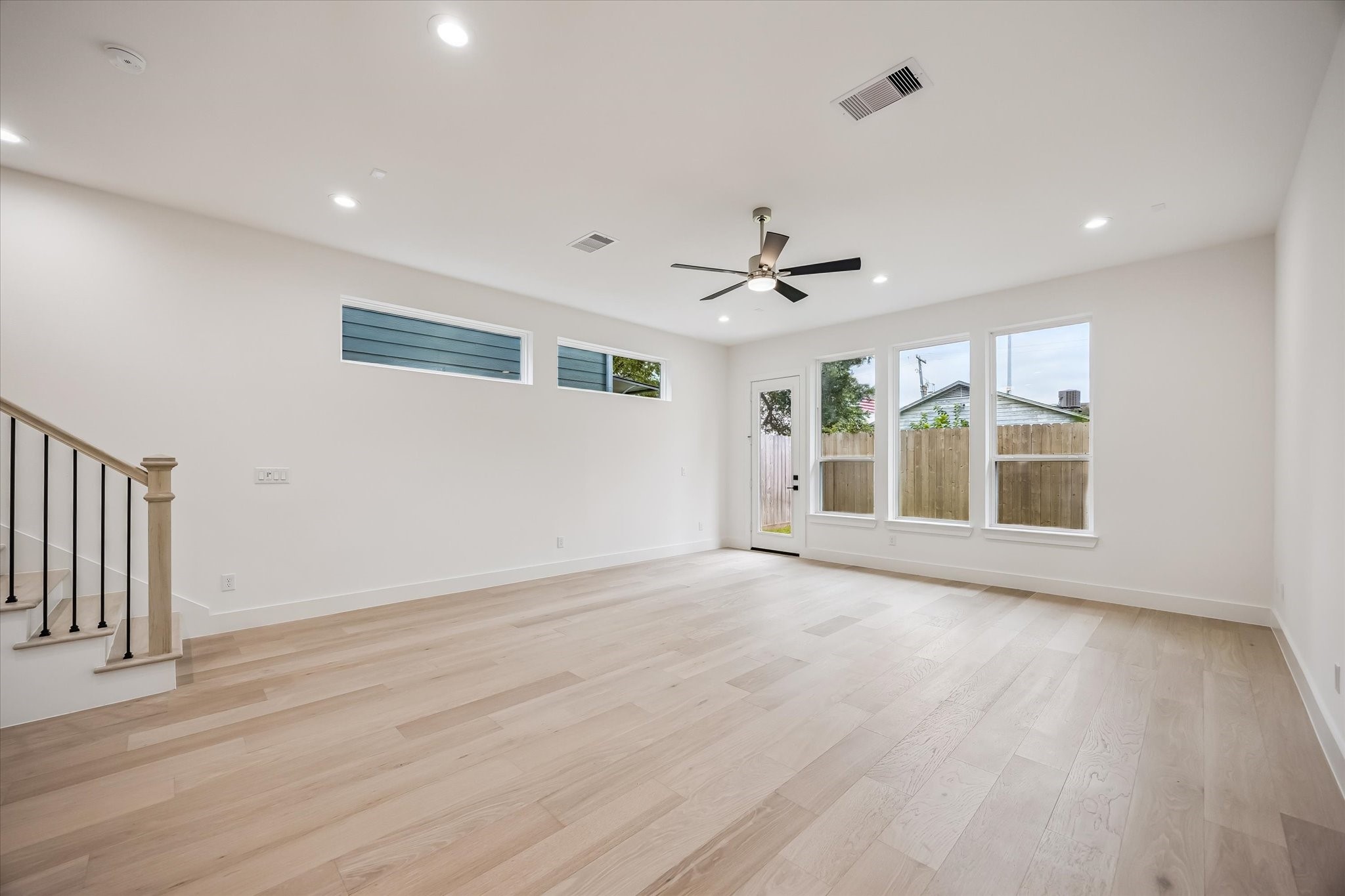 Spacious, light-filled living area with sleek hardwood floors, modern ceiling fan, and large windows offering backyard views.