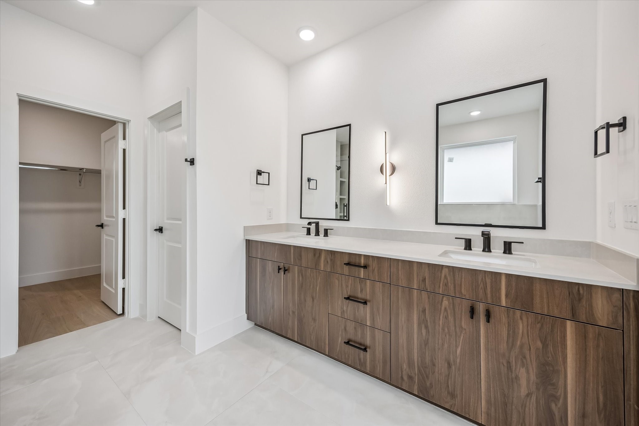 Spacious modern bathroom featuring a dual-sink vanity with sleek fixtures, elegant mirrors, and ample storage, complemented by a walk-in closet for convenience.
