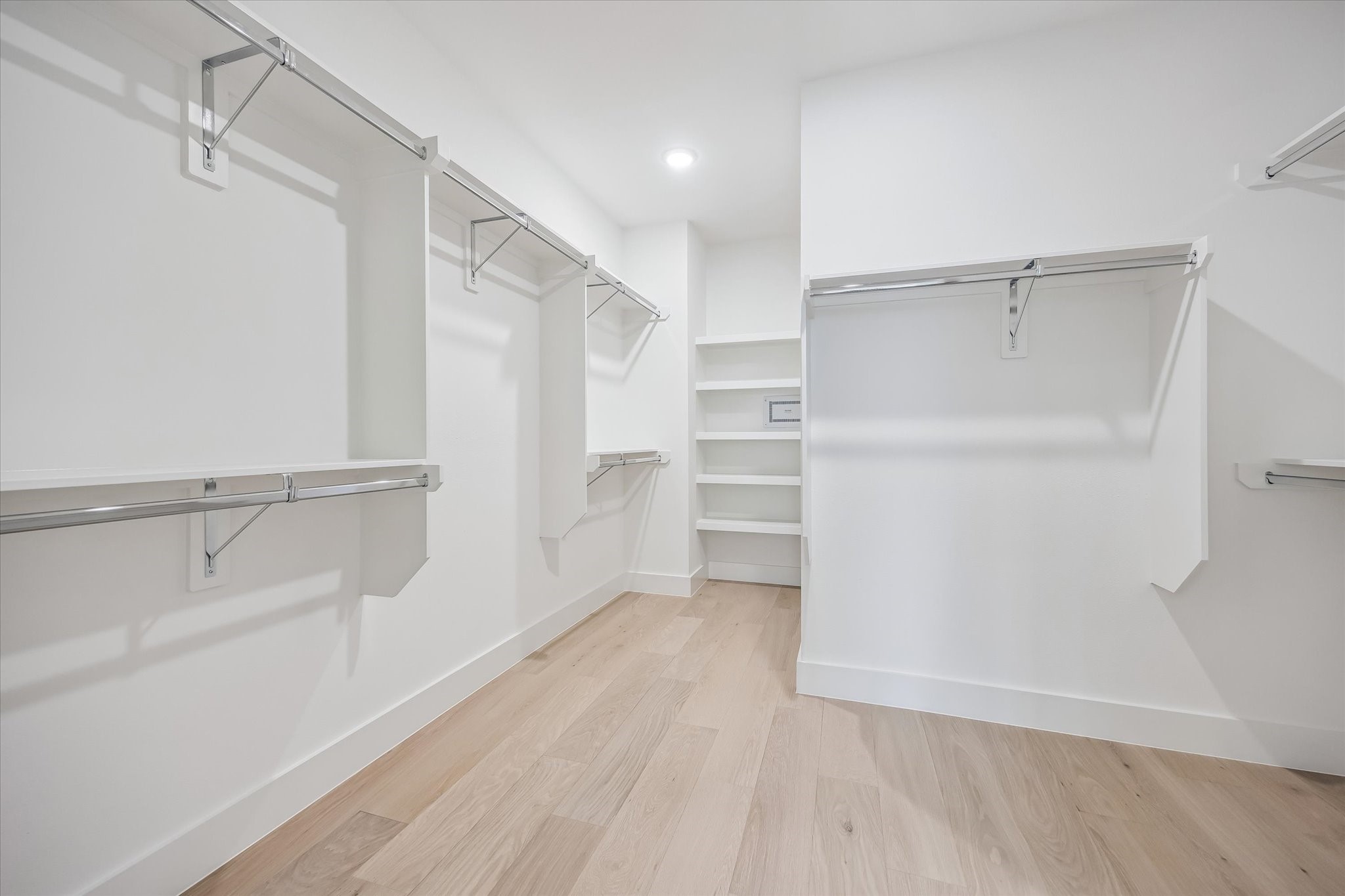 Spacious walk-in closet featuring ample hanging space, sleek shelving, and modern light wood flooring for a clean, organized look.