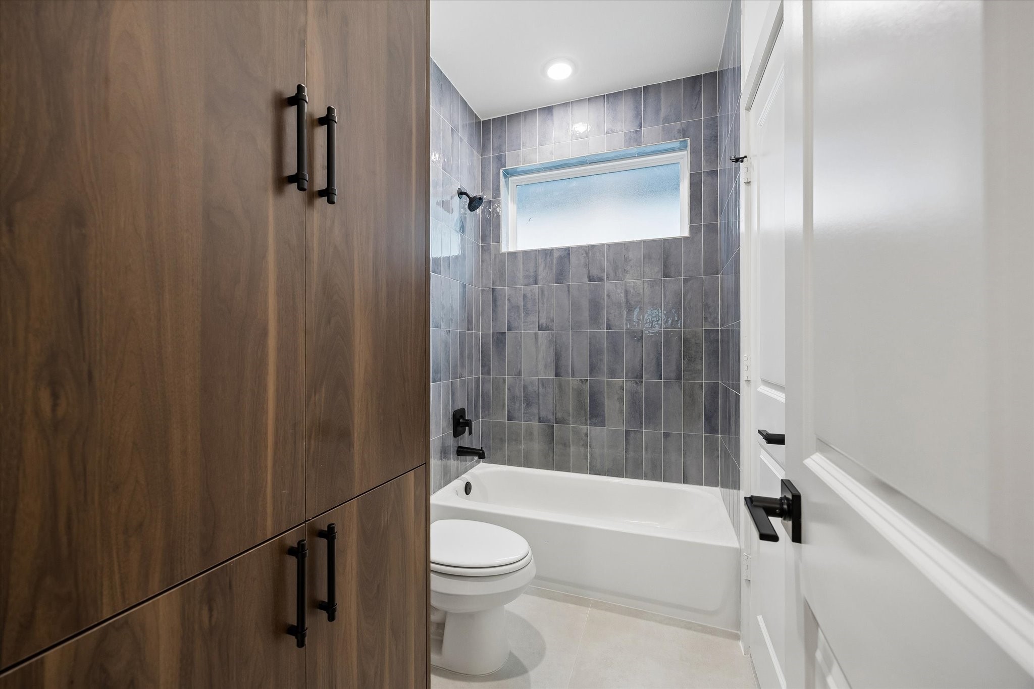 Stylish bathroom featuring modern grey tile, a sleek bathtub-shower combo, and ample wooden cabinetry for storage.