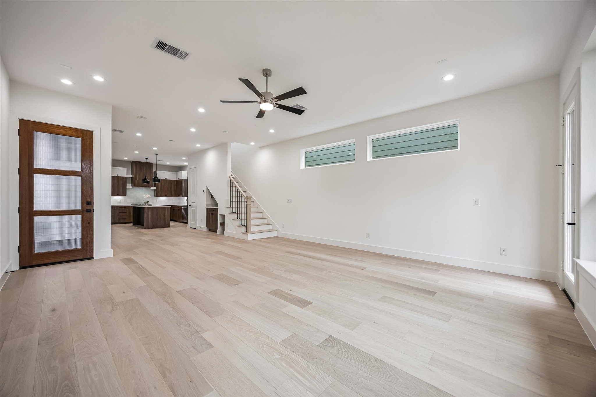 Spacious open-concept living area with light wood flooring and modern finishes, featuring a stylish kitchen with dark cabinetry, sleek countertops, and a ceiling fan for added comfort.