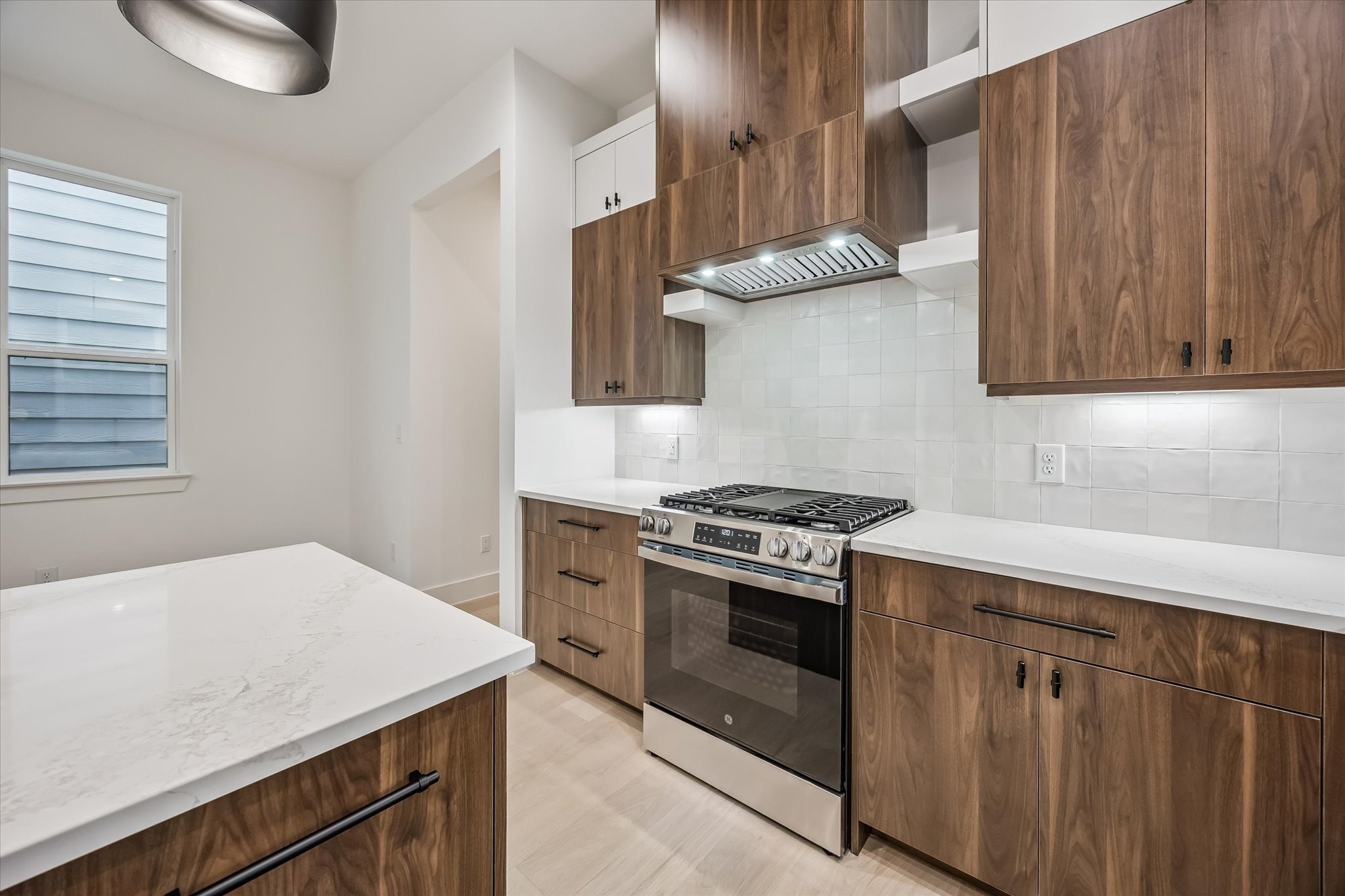 Modern kitchen with sleek wood cabinetry, a stainless steel gas range, and elegant white countertops.