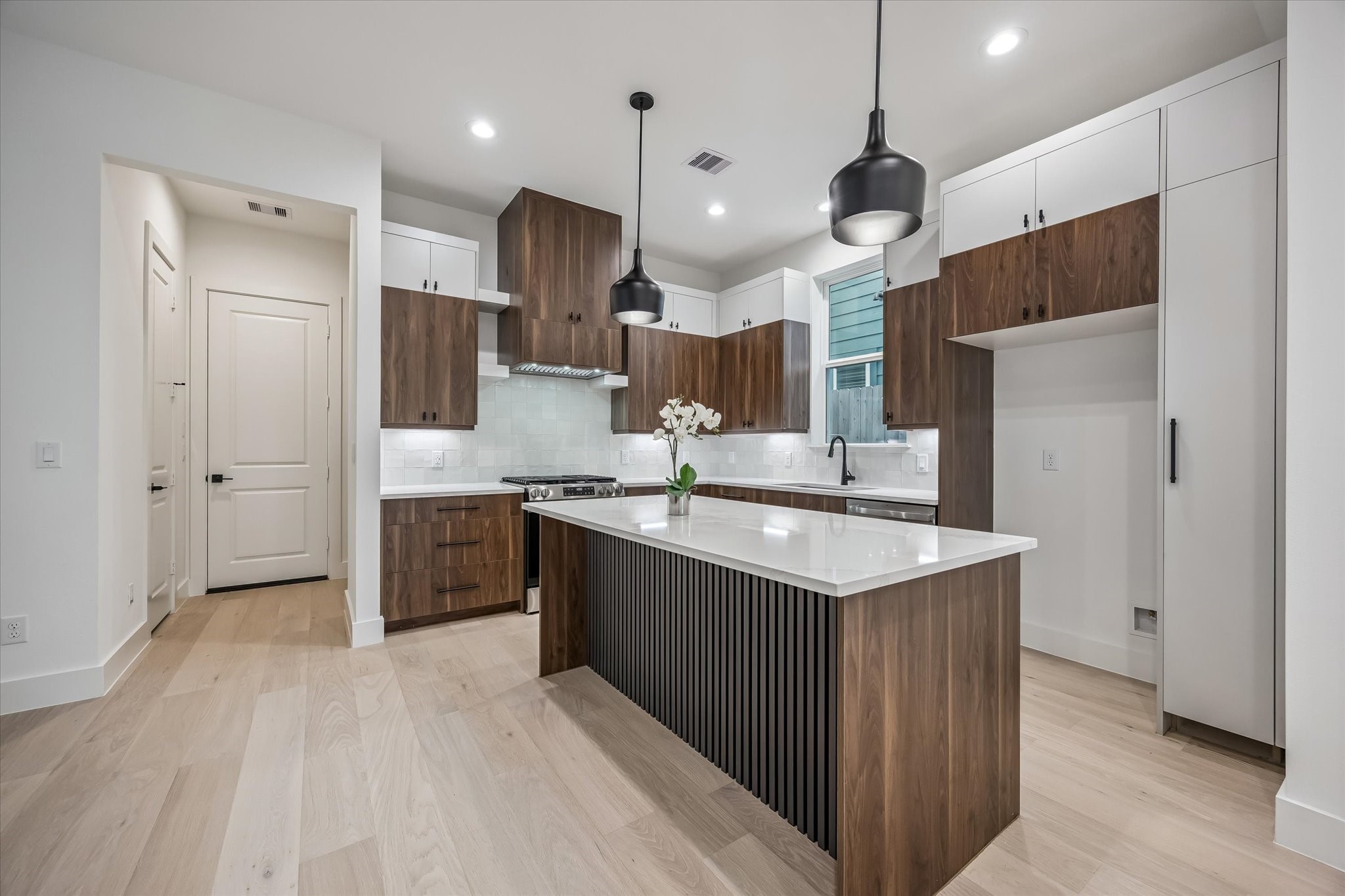 Sleek modern kitchen with elegant wood cabinetry and a spacious island, complemented by contemporary pendant lighting and light wood flooring.