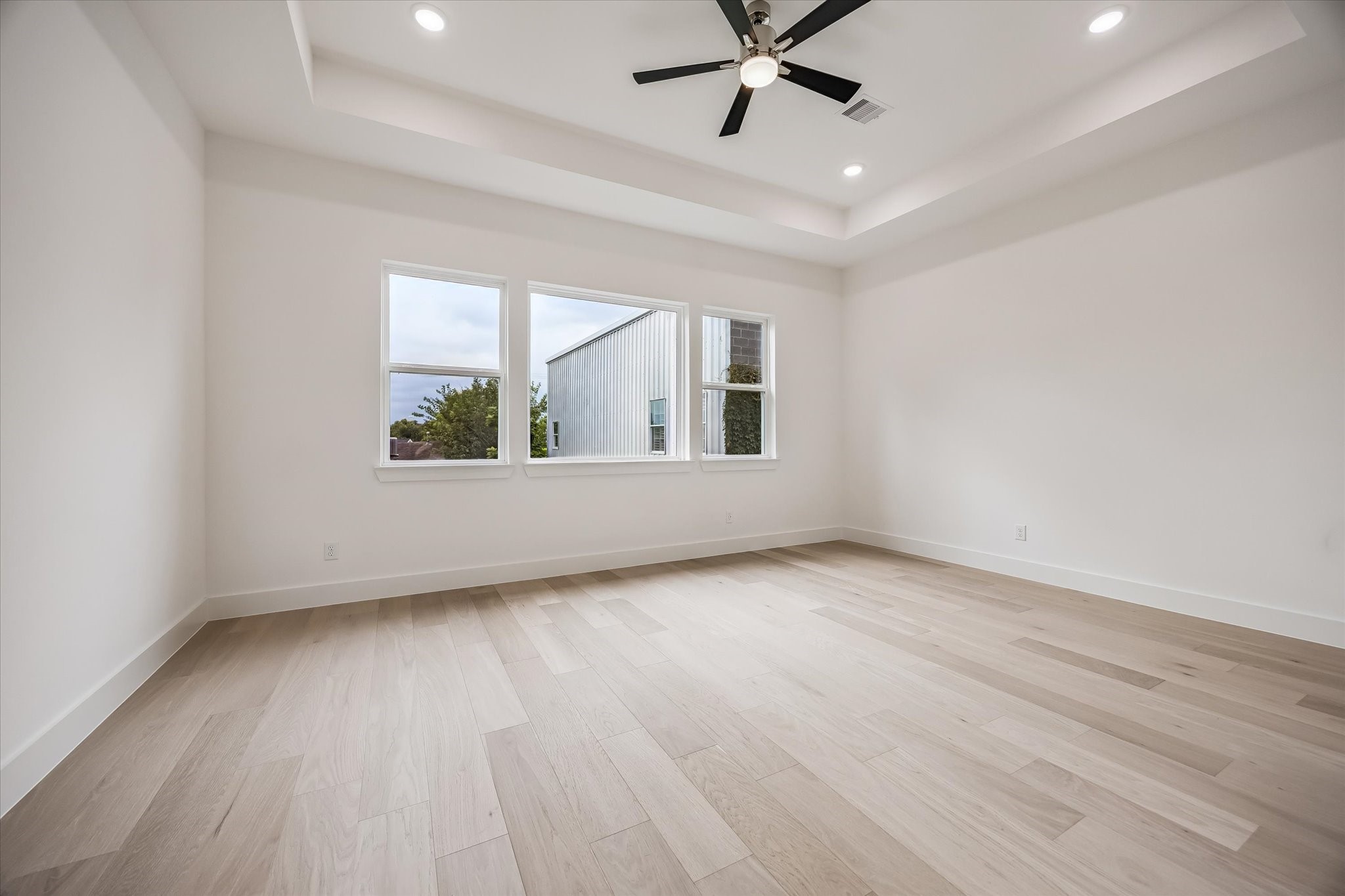 Spacious and bright room featuring light wood flooring, large windows, and a modern ceiling fan with recessed lighting.