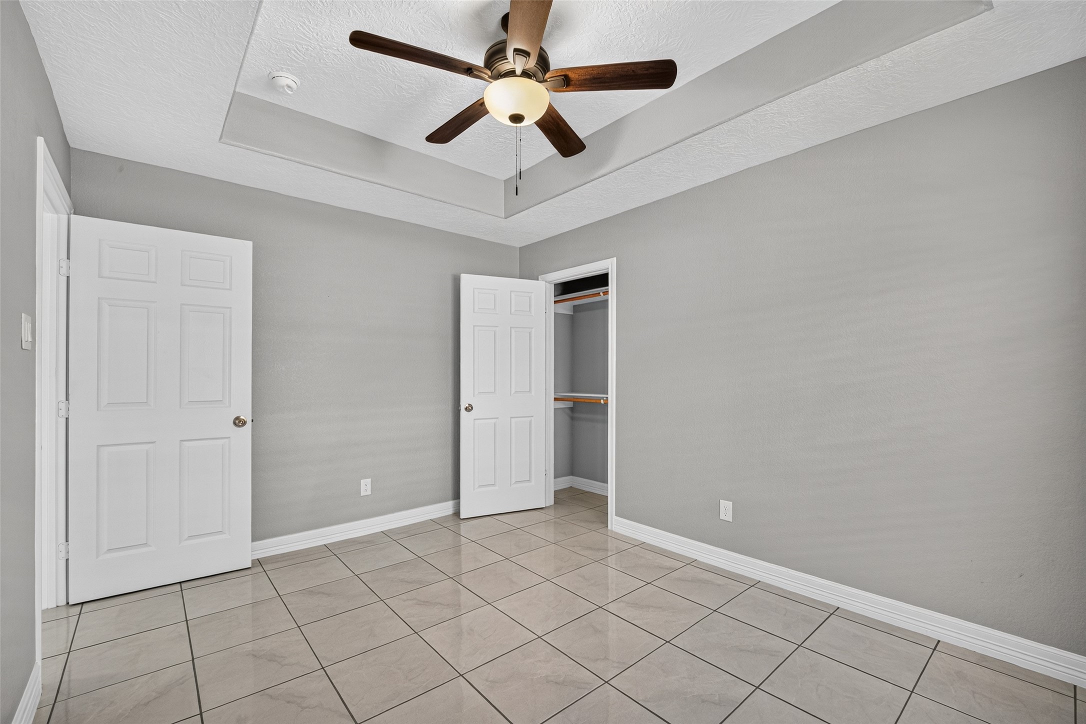 Bright and spacious room featuring a modern ceiling fan, elegant tray ceiling, and sleek tile flooring.