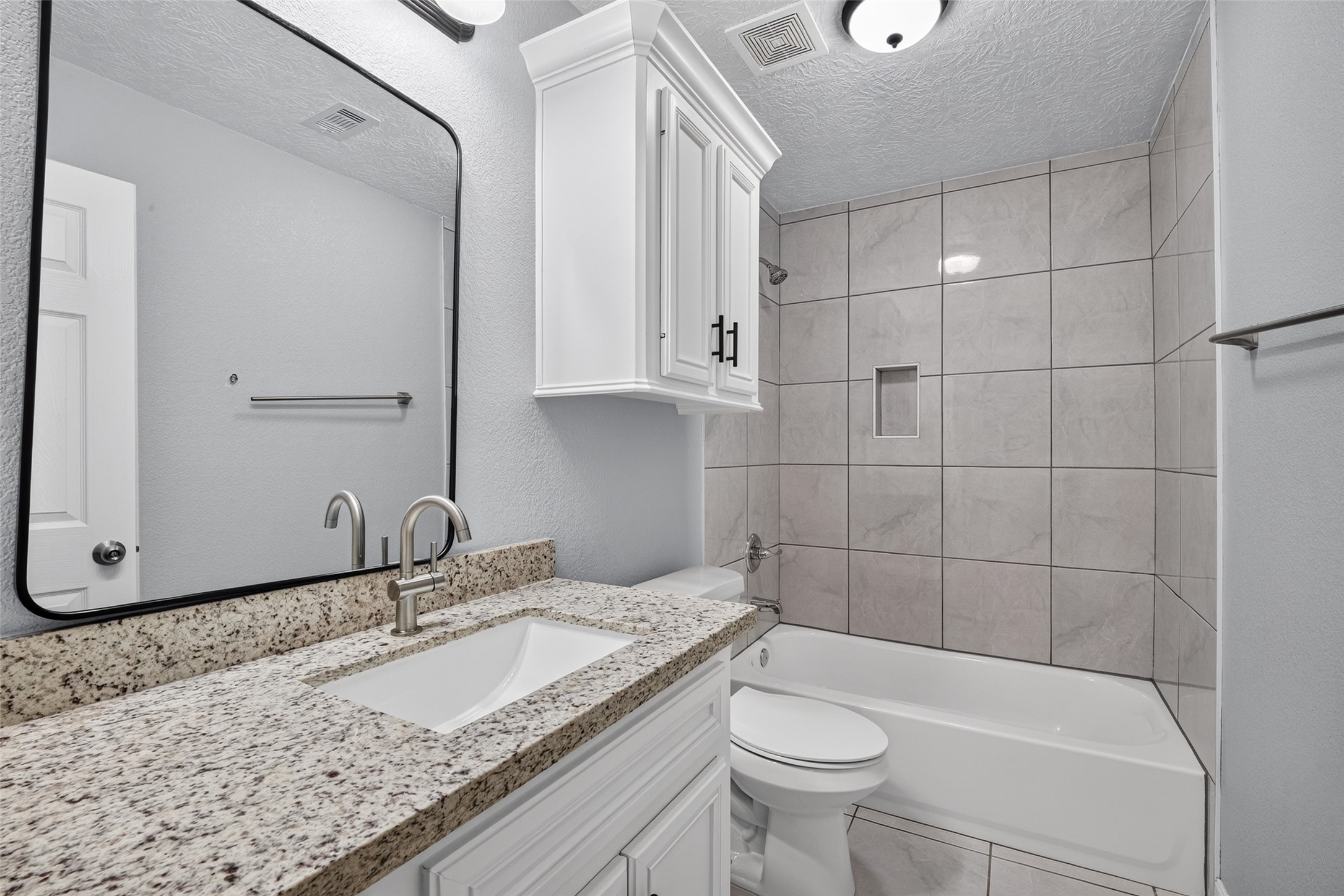 Modern bathroom featuring a sleek granite countertop, elegant tile backsplash, and a convenient shower-tub combination.