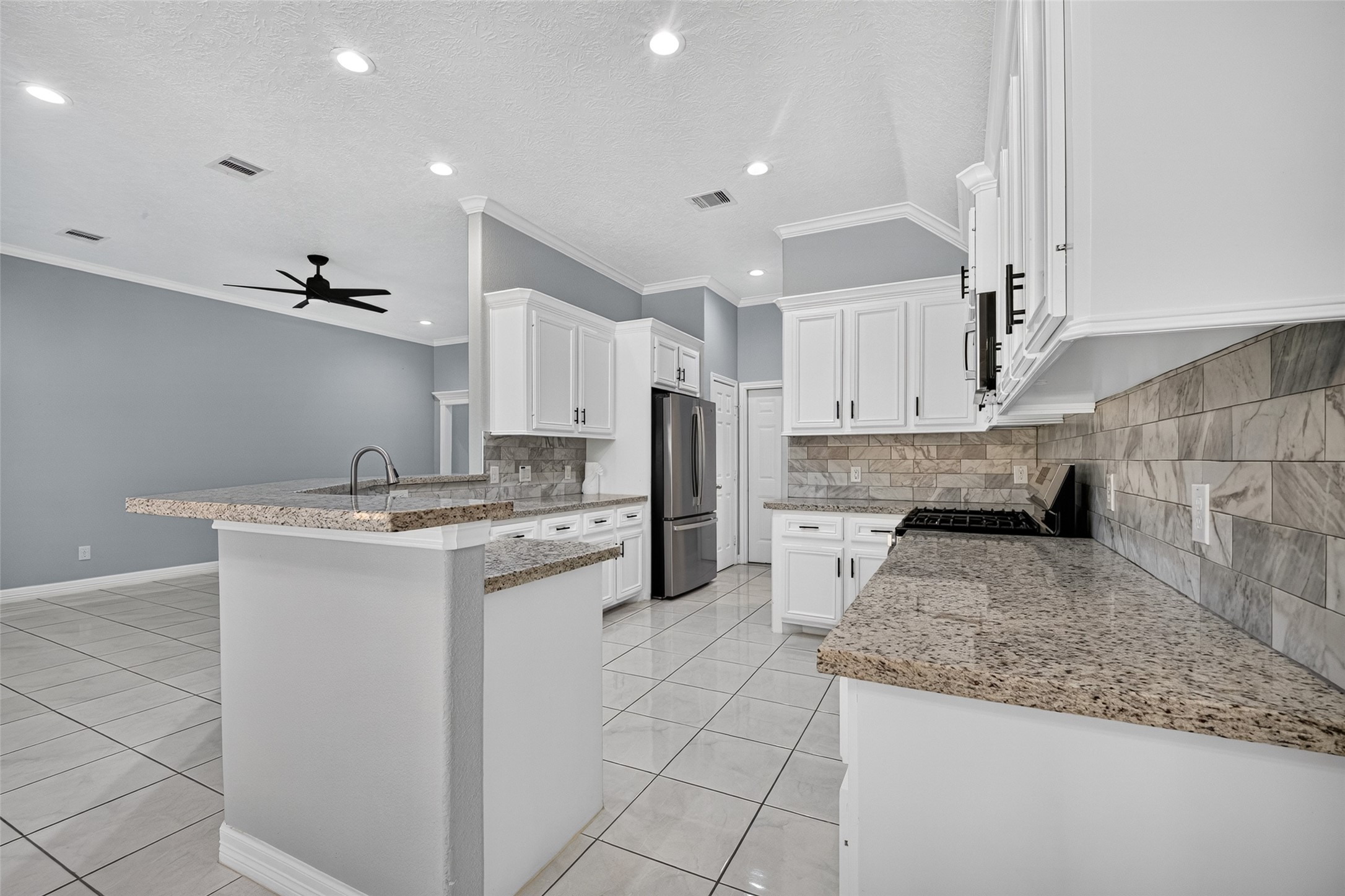 Spacious kitchen with modern stainless steel appliances, elegant granite countertops, and sleek white cabinetry, seamlessly flowing into an open living area with high ceilings and recessed lighting.
