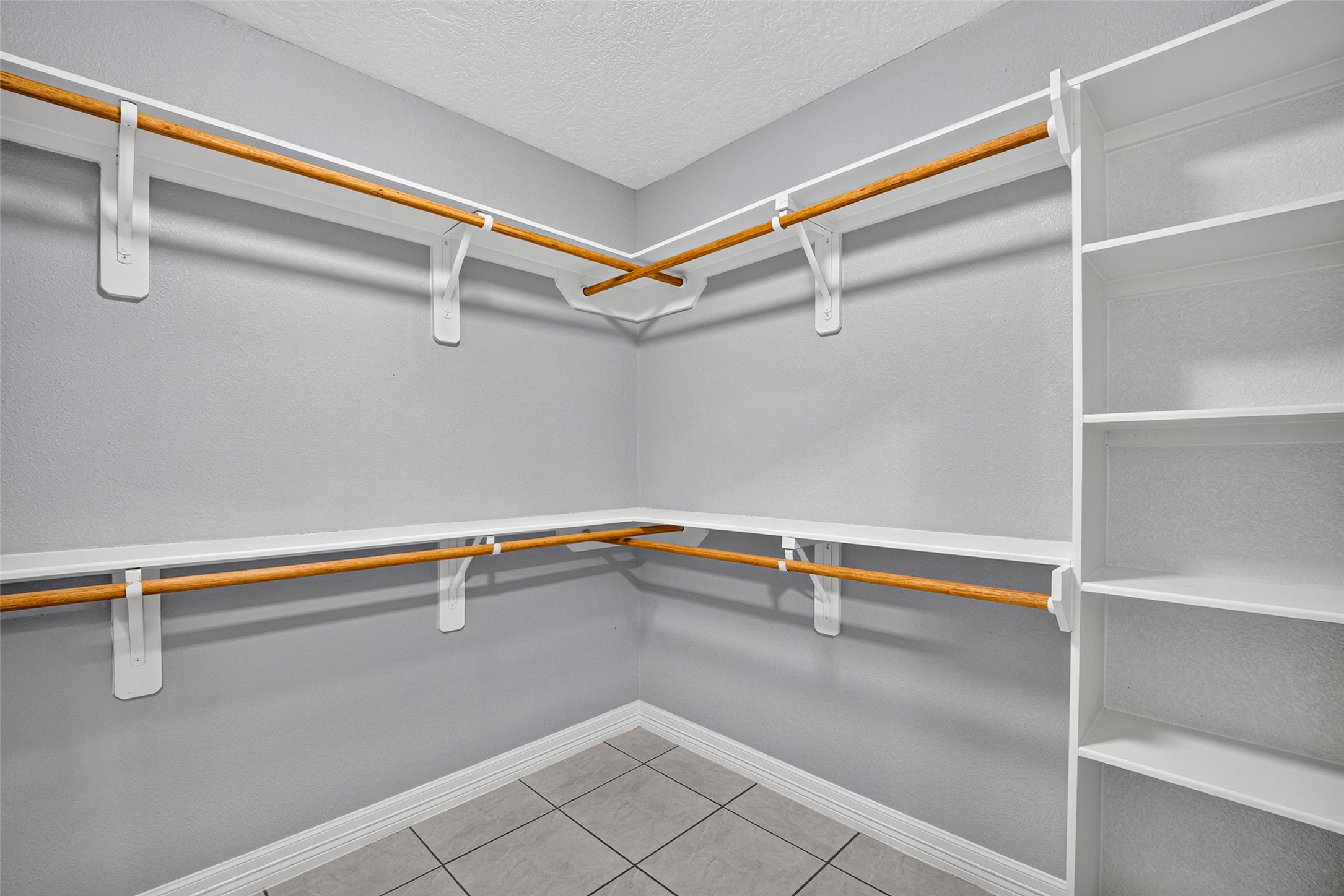 Spacious walk-in closet with ample shelving and hanging space, featuring a neutral color palette and tile flooring for a clean, organized look.