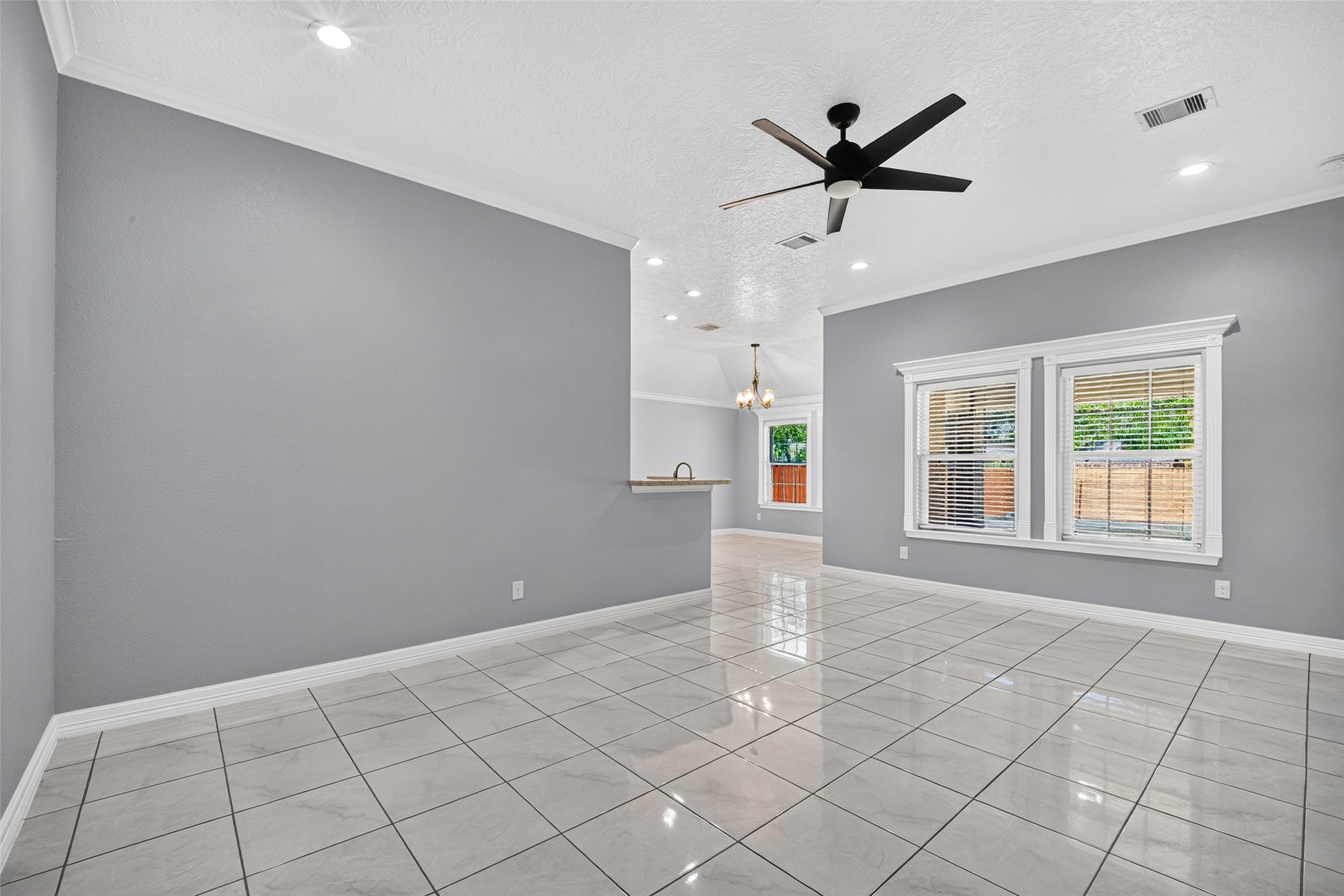 Bright and spacious living area with sleek tile flooring, modern ceiling fan, and large windows for ample natural light, seamlessly flowing into an open kitchen with elegant finishes. Bright and spacious living area with sleek tile flooring, modern ceiling fan, and large windows for ample natural light, seamlessly flowing into an open kitchen with elegant finishes.