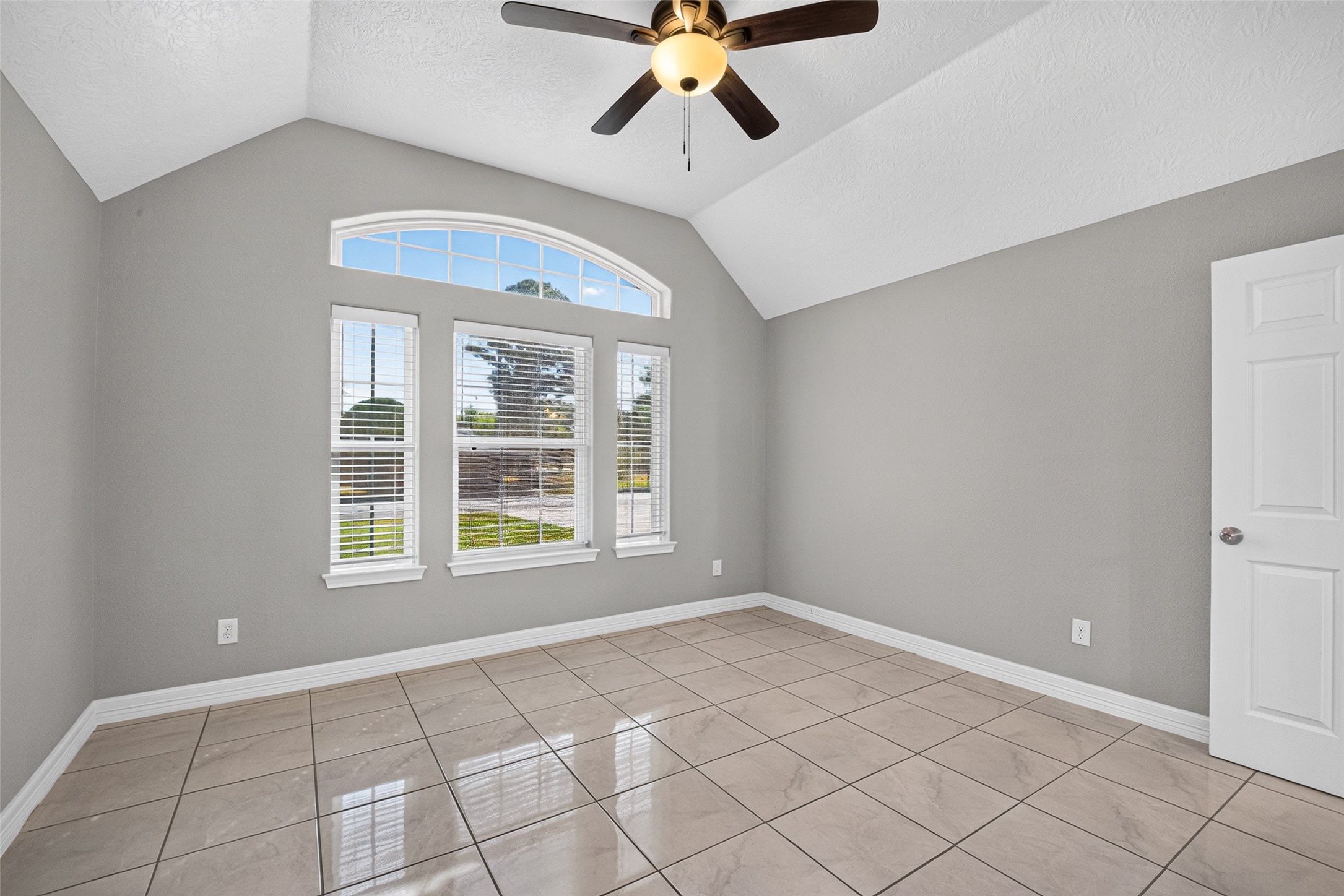 Bright and inviting secondary bedroom featuring a high ceiling, elegant tile flooring, and a large arched window that fills the space with natural light.