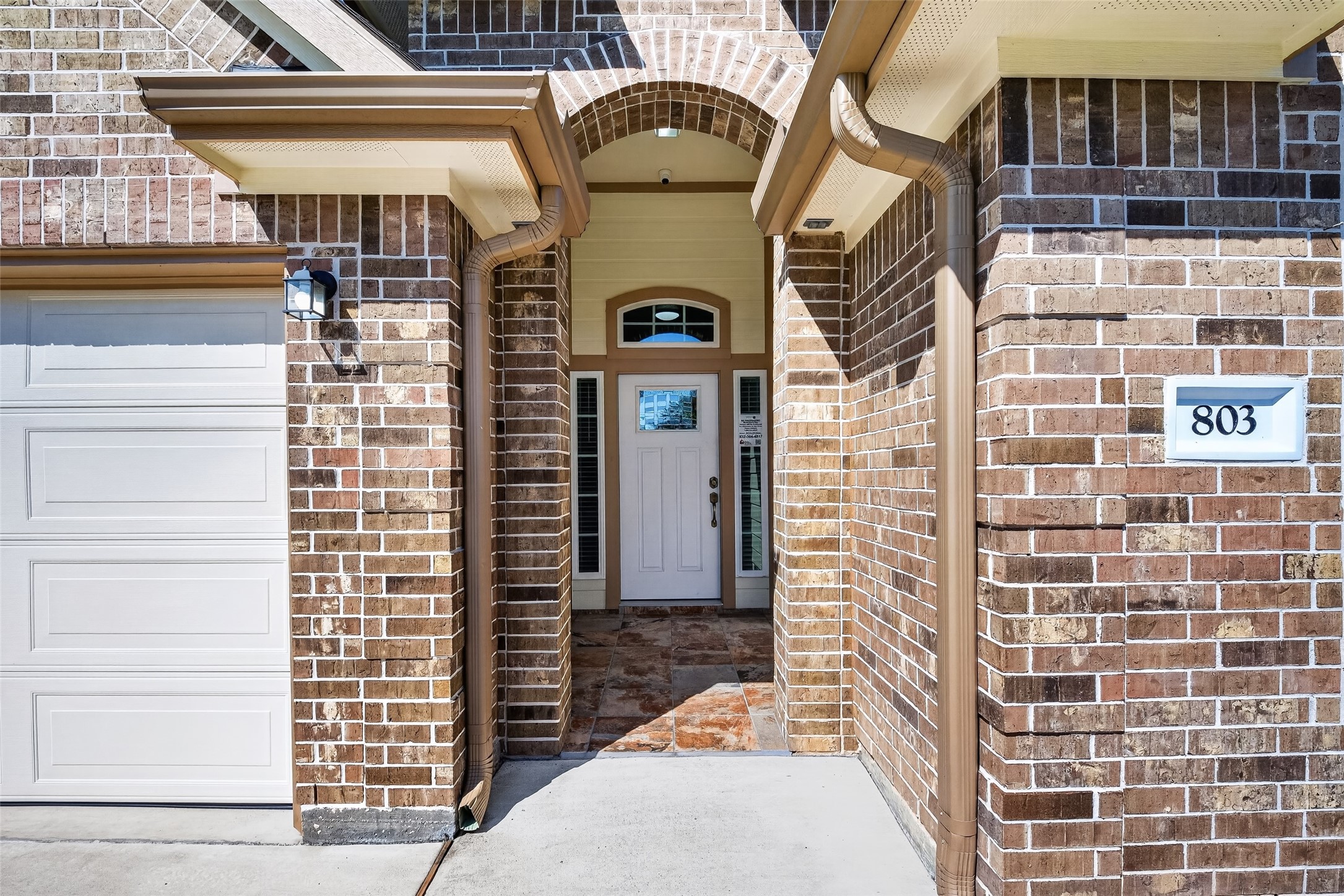 Charming brick exterior with a welcoming arched entryway, complemented by a classic white door and adjacent garage. Charming brick exterior with a welcoming arched entryway, complemented by a classic white door and adjacent garage.