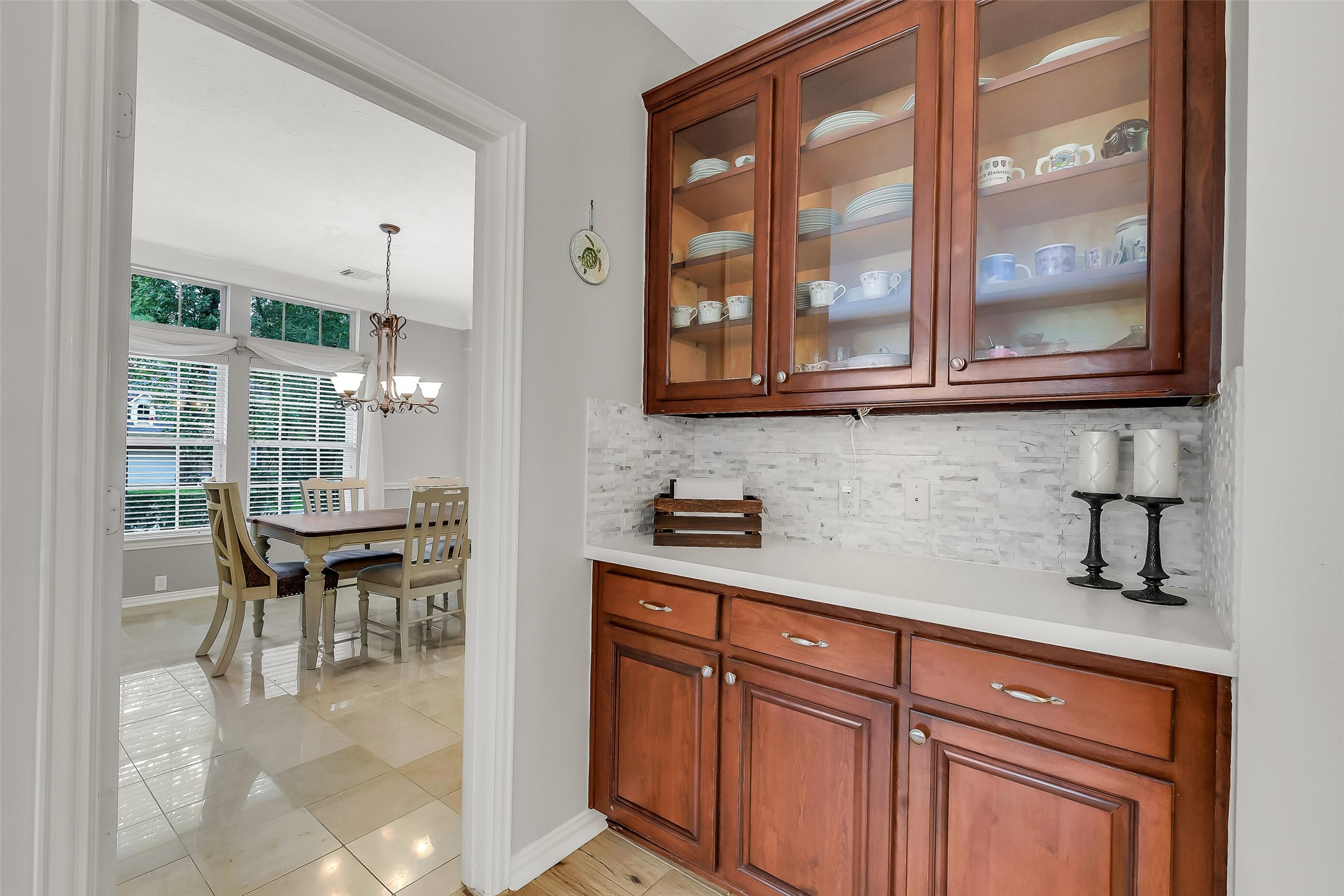 Featuring rich wood cabinetry and glass doors, leading to a bright dining space with large windows and a stylish chandelier.