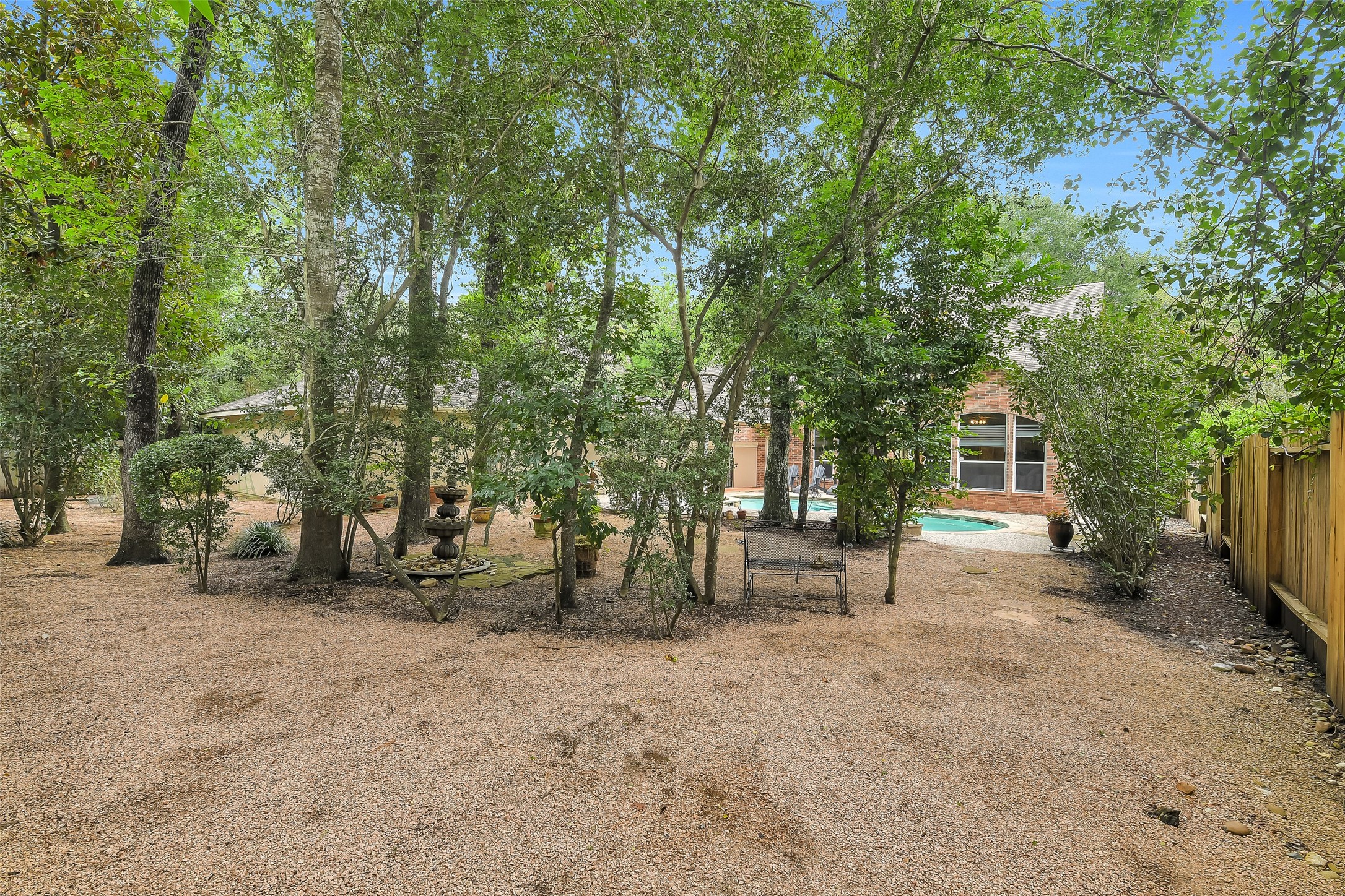 Serene backyard oasis with lush trees, a charming fountain, and a private pool, perfect for relaxation and outdoor enjoyment.