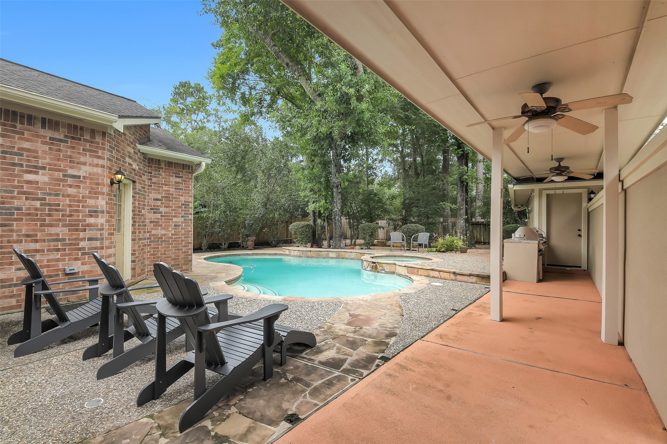 Discover a serene backyard oasis featuring a sparkling pool surrounded by lush greenery. Enjoy outdoor relaxation on the covered patio with ceiling fans and ample seating, perfect for entertaining or unwinding in tranquility.