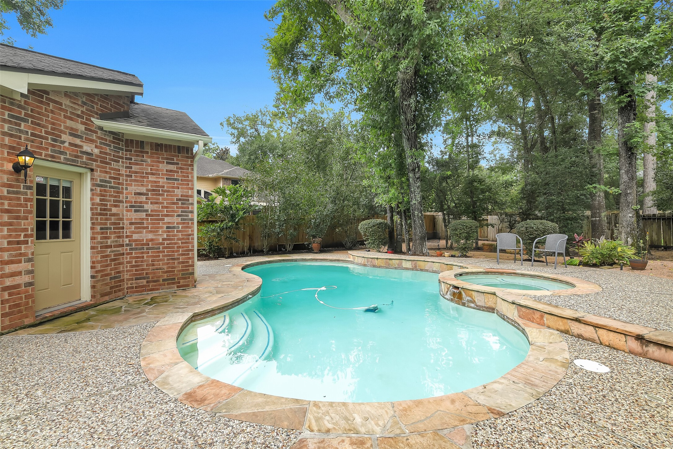 Charming backyard oasis featuring a sparkling pool and spa, surrounded by lush greenery and a patio perfect for relaxing or entertaining.