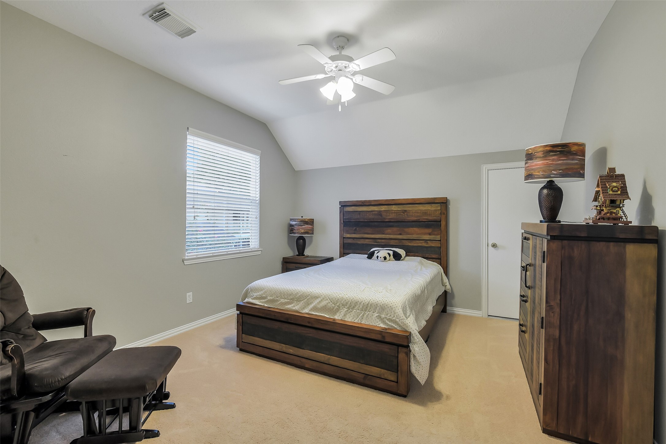 Spacious Guest bedroom featuring a cozy bed with rustic wood furniture, neutral walls, and a ceiling fan for added comfort.