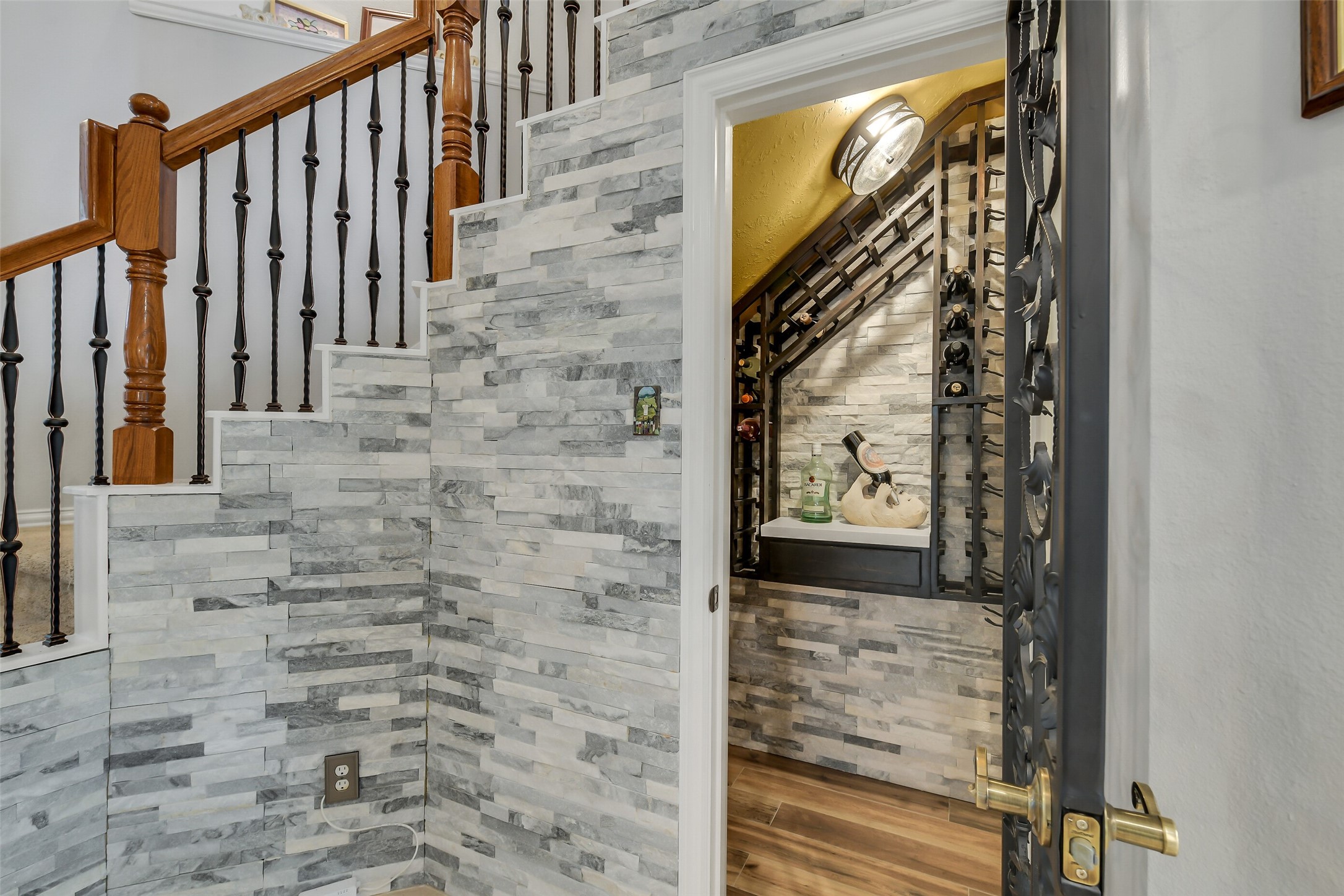 Charming under-stair wine cellar features elegant stone walls and stylish iron door, perfect for wine enthusiasts.