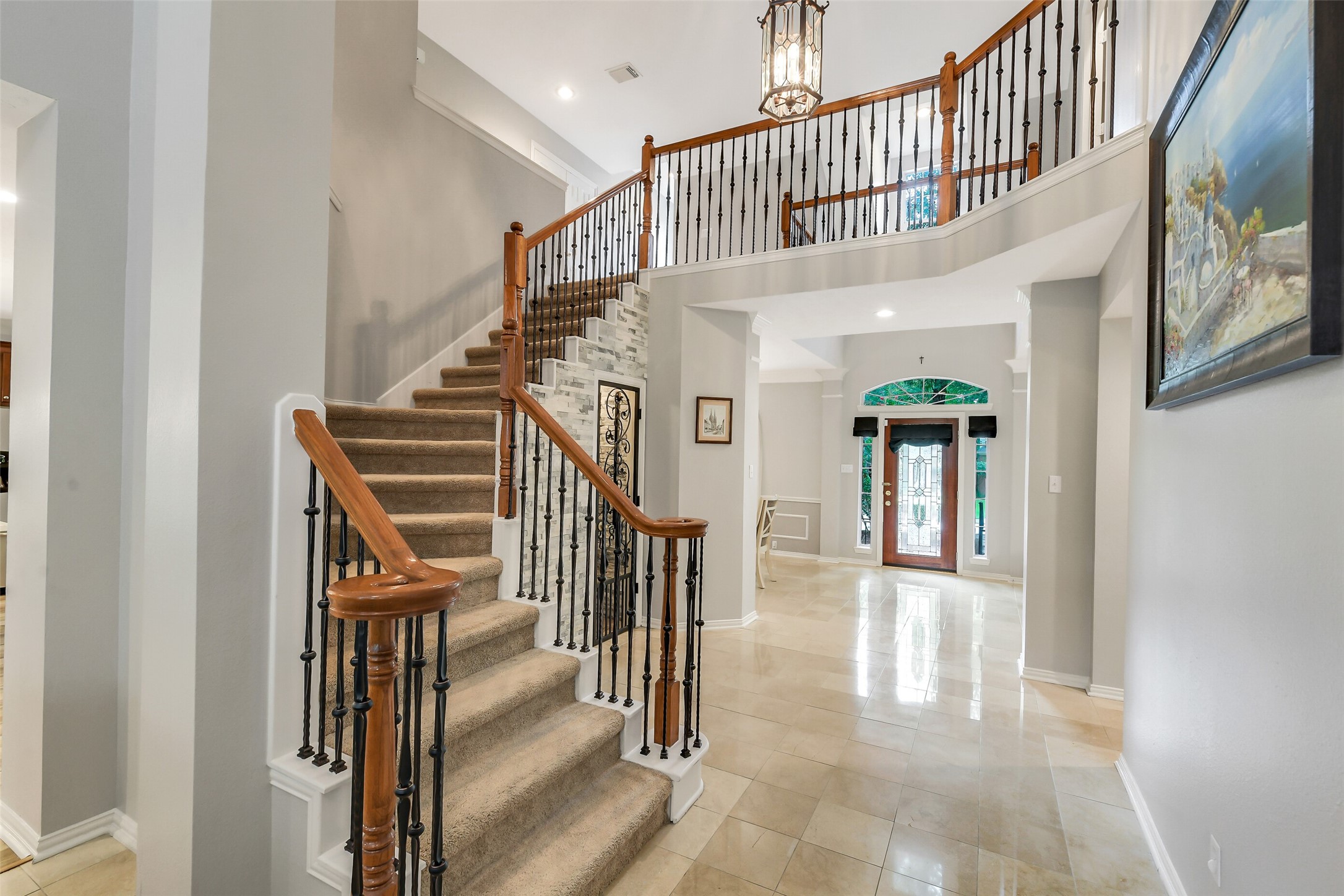 Elegant foyer featuring a grand staircase with wrought iron spindles, polished tile floors, and a welcoming grand-door entrance.