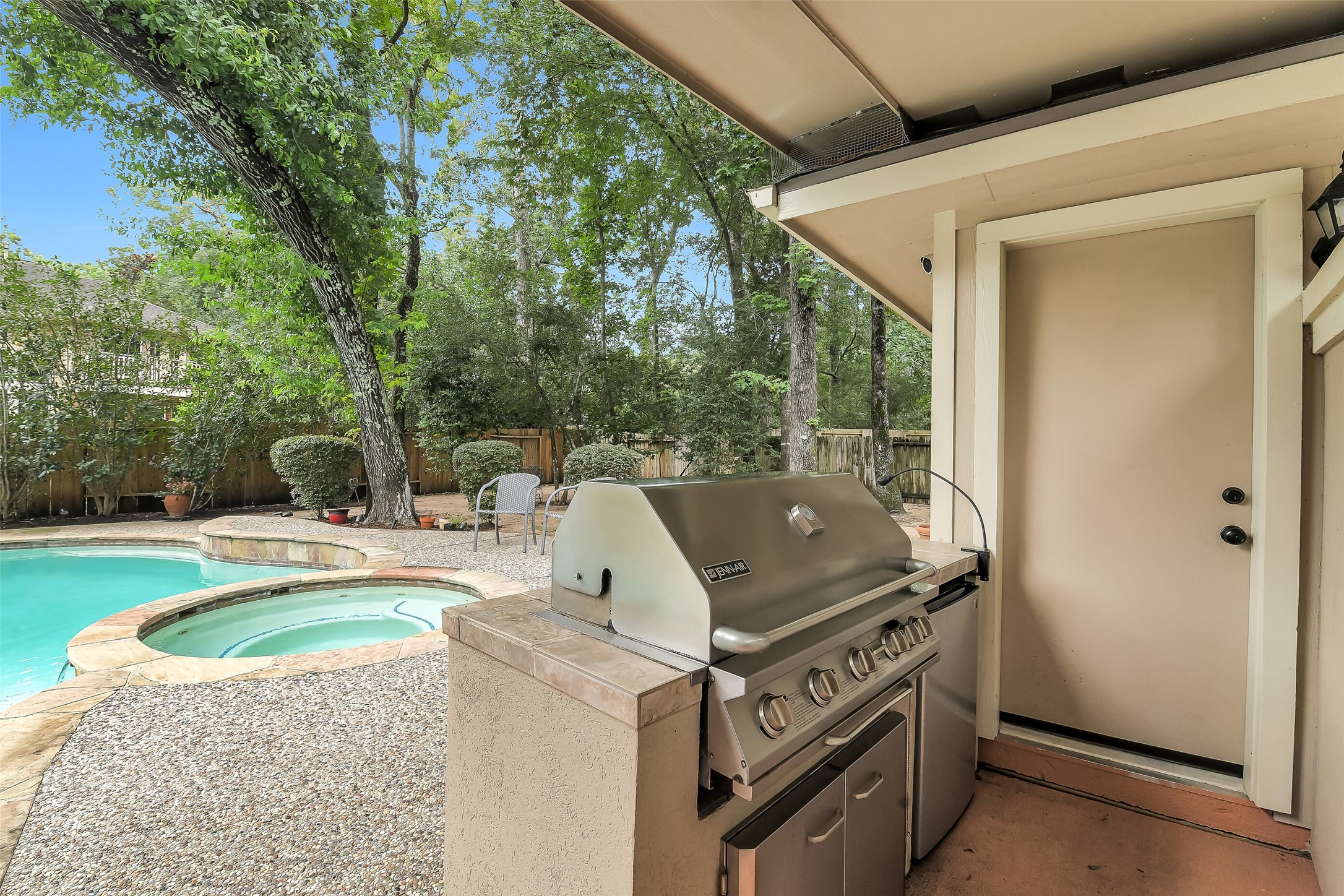 Enjoy outdoor living with a built-in grill overlooking a sparkling pool and spa, surrounded by lush greenery for a private retreat.
