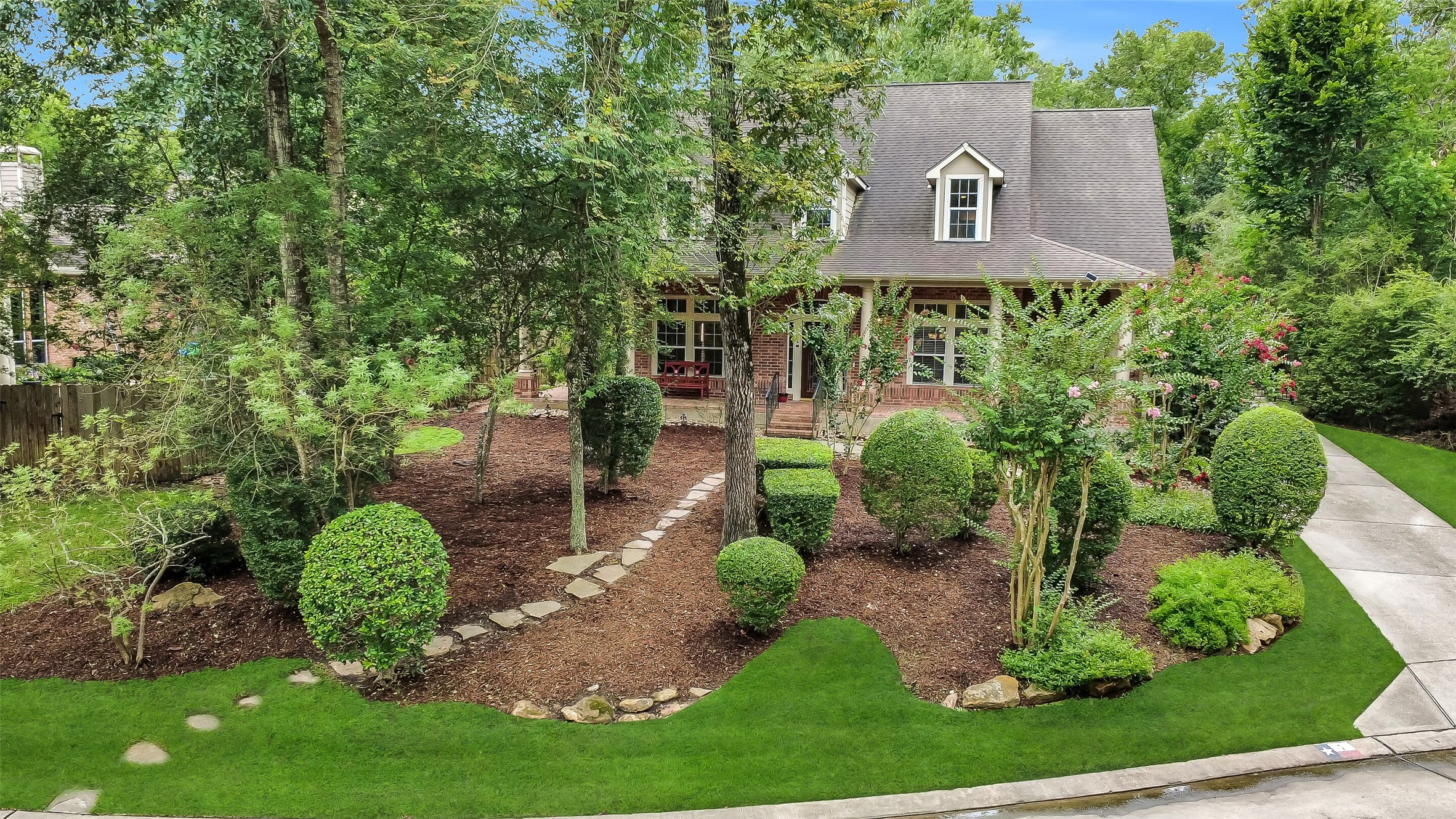 Charming two-story home nestled among mature trees, featuring a beautifully landscaped front yard with a stone path leading to a welcoming porch.