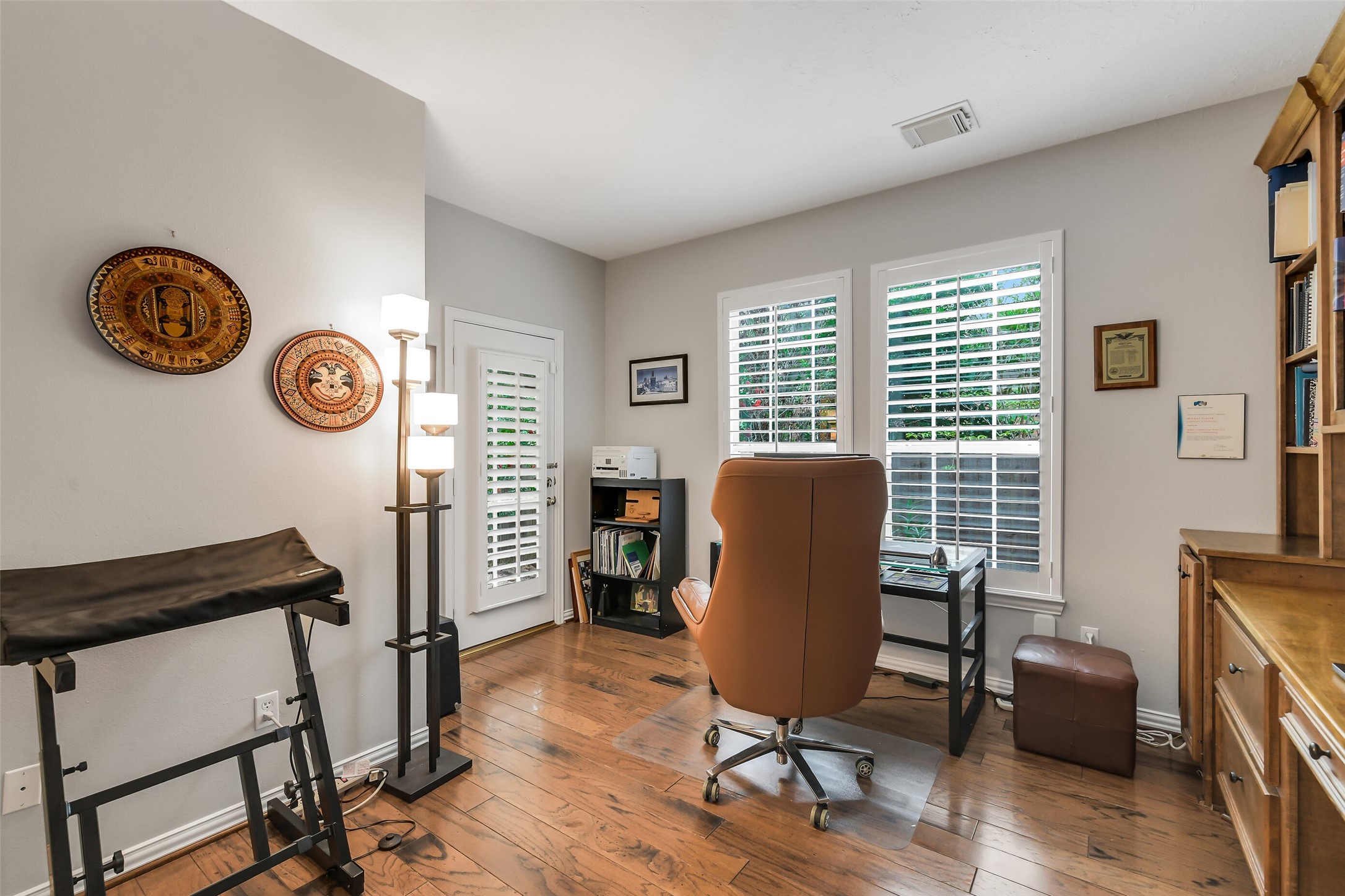 Home office featuring hardwood floors, abundant natural light through large windows with shutters, and ample space for a comfortable workspace setup. Has seperate entrance to front verandah.