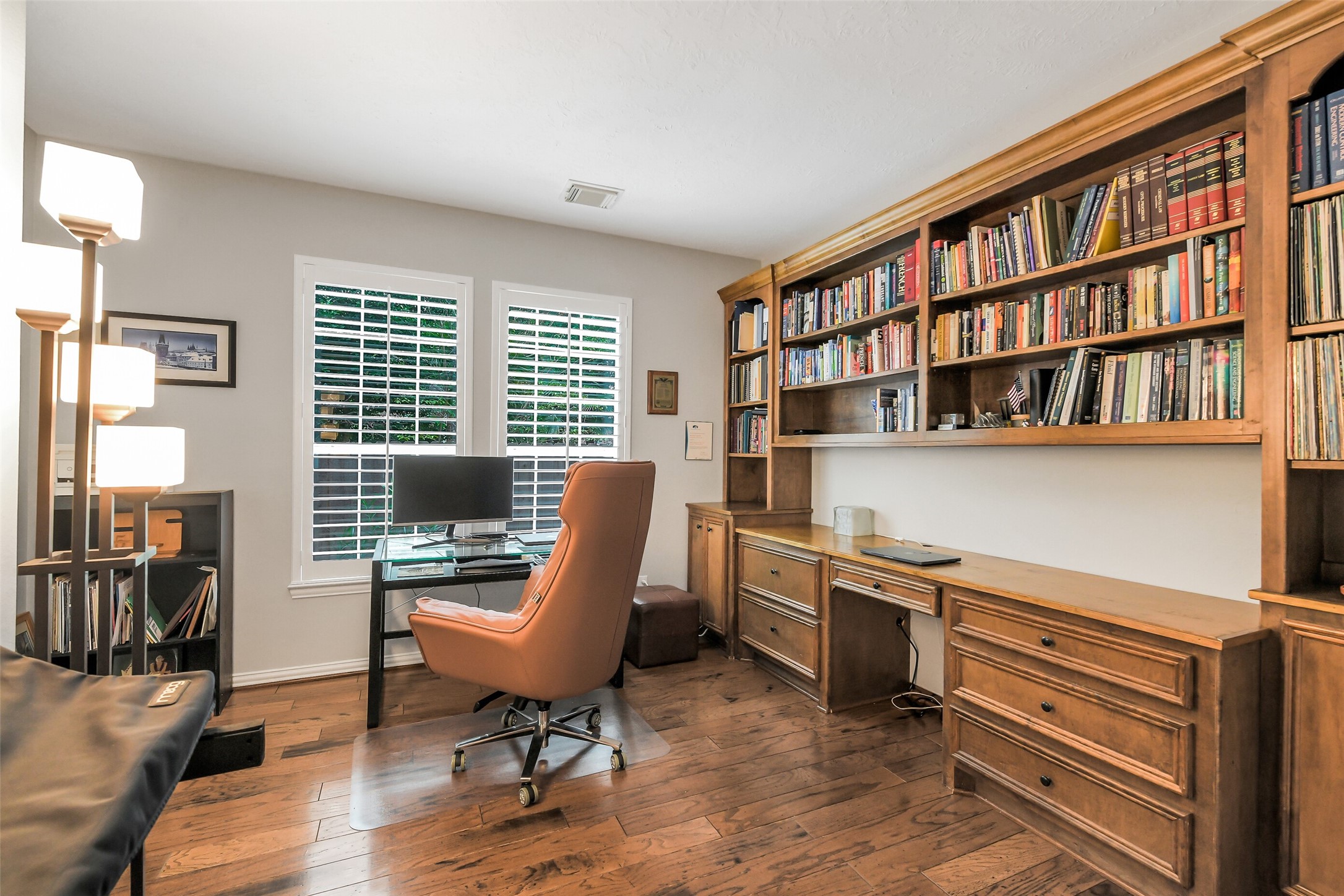 Elegant home office with rich wood flooring, built-in bookshelves, and ample natural light from large windows, offering a perfect space for work and study.
